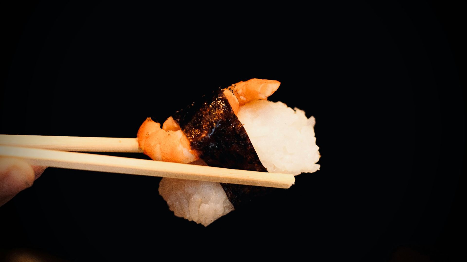 a person holding a piece of sushi with chopsticks