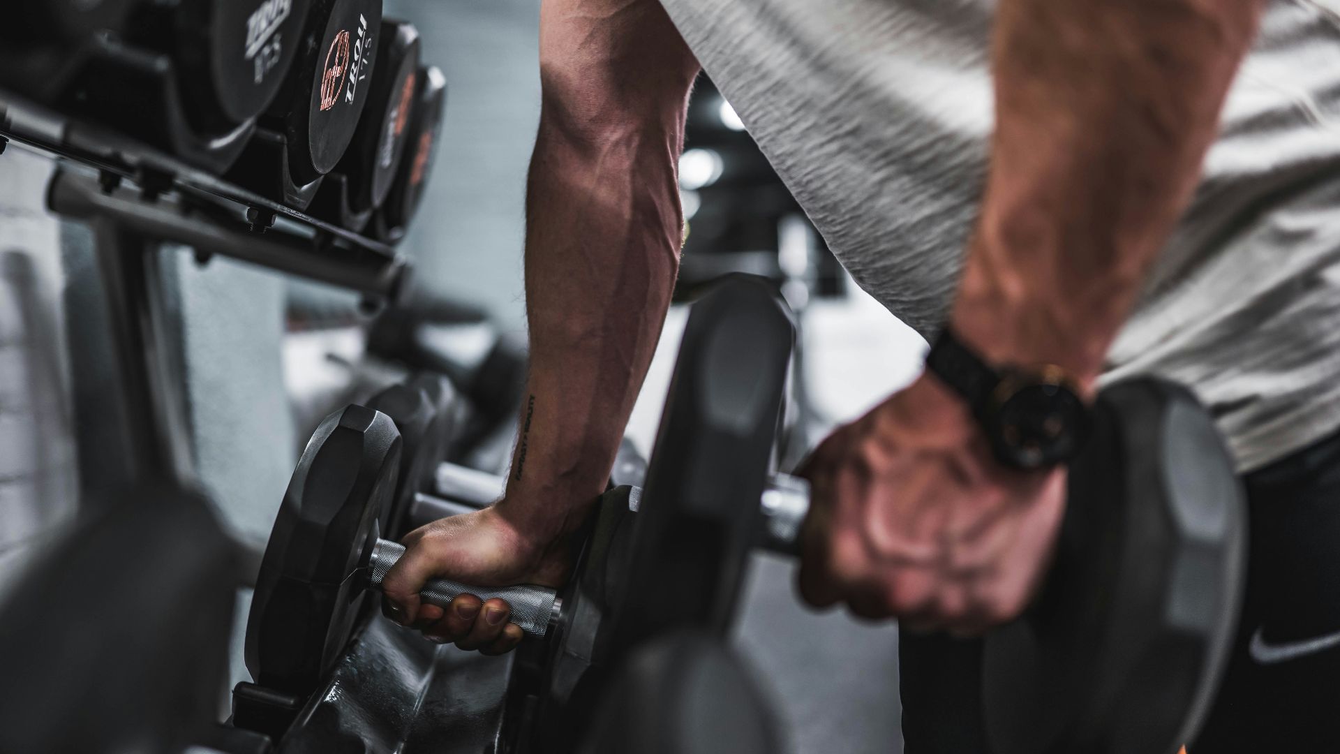 person in gray shirt holding black dumbbell