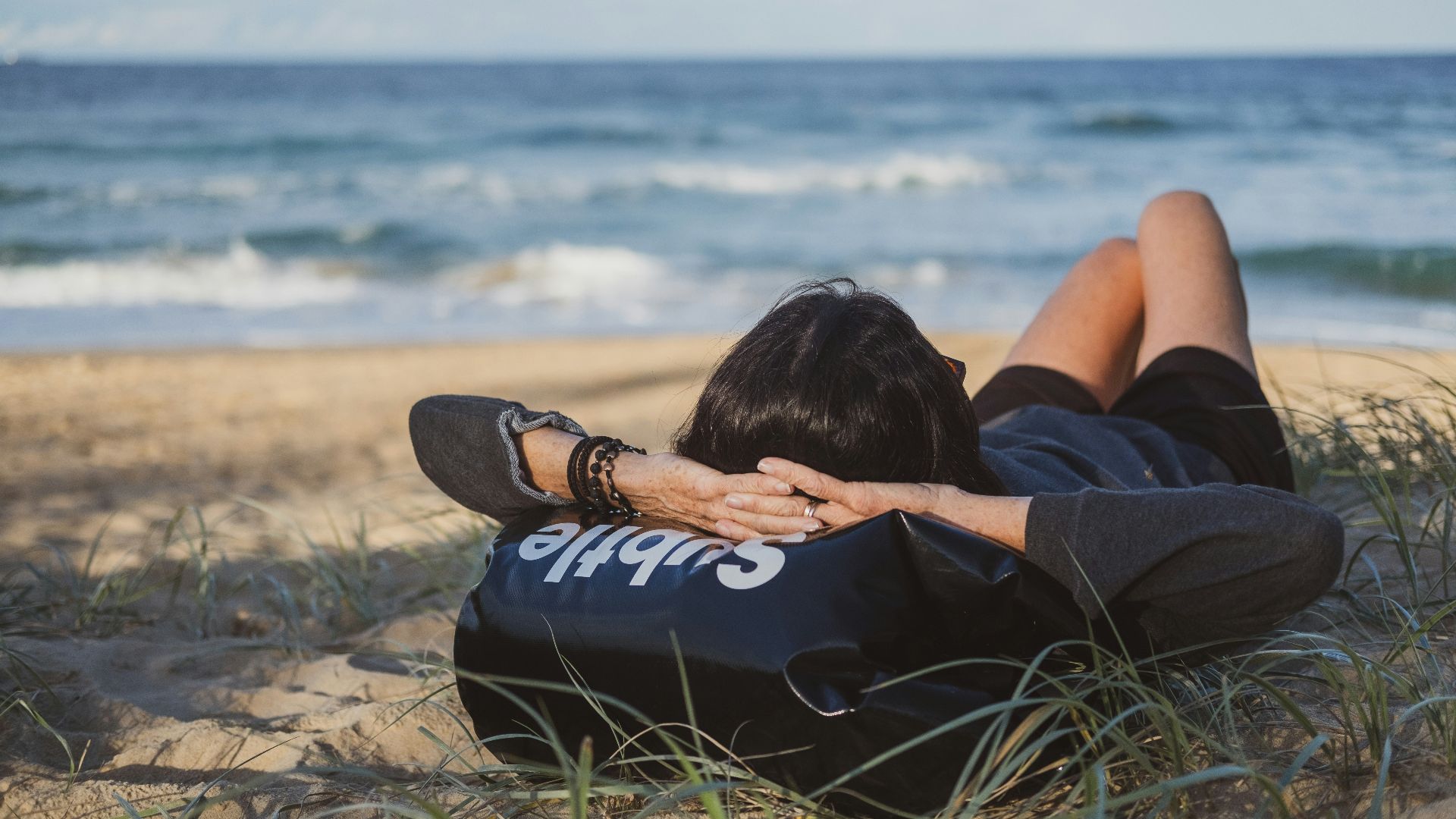 woman lying on grass front of sea at daytime