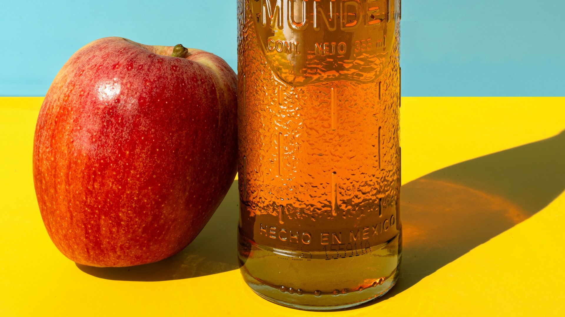 A bottle of apple cider next to an apple