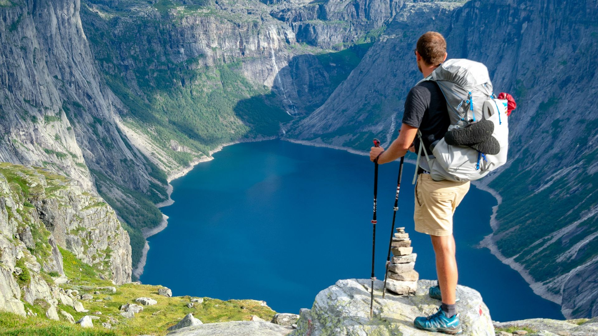 man standing on rock looking towards lake