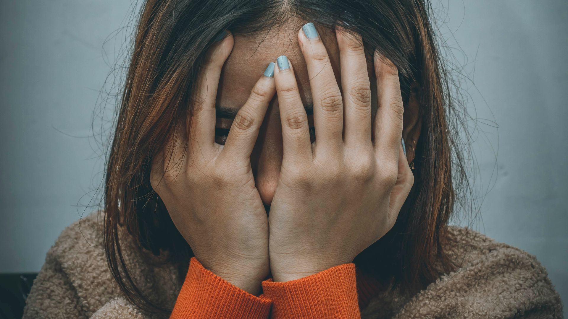 woman in brown sweater covering her face with her hand