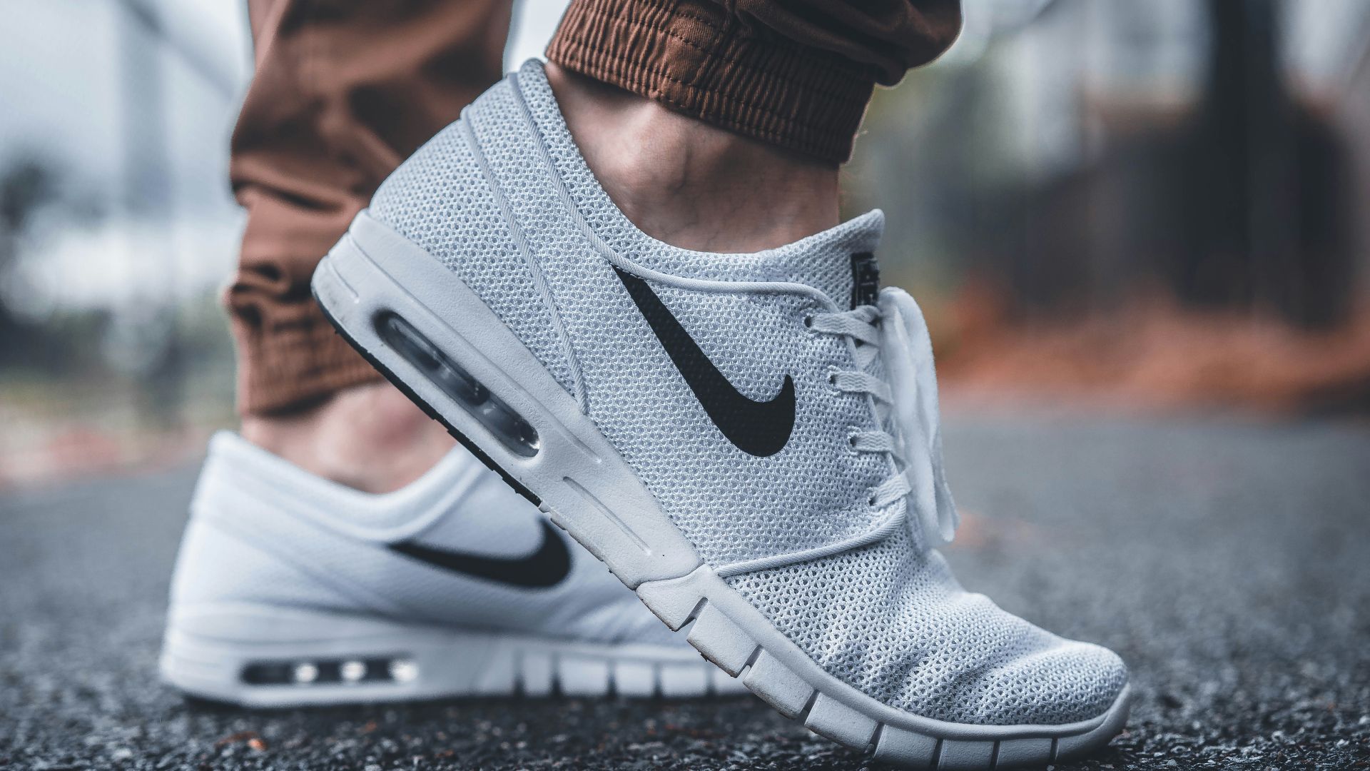 person wearing white Nike running shoes standing on black concrete path