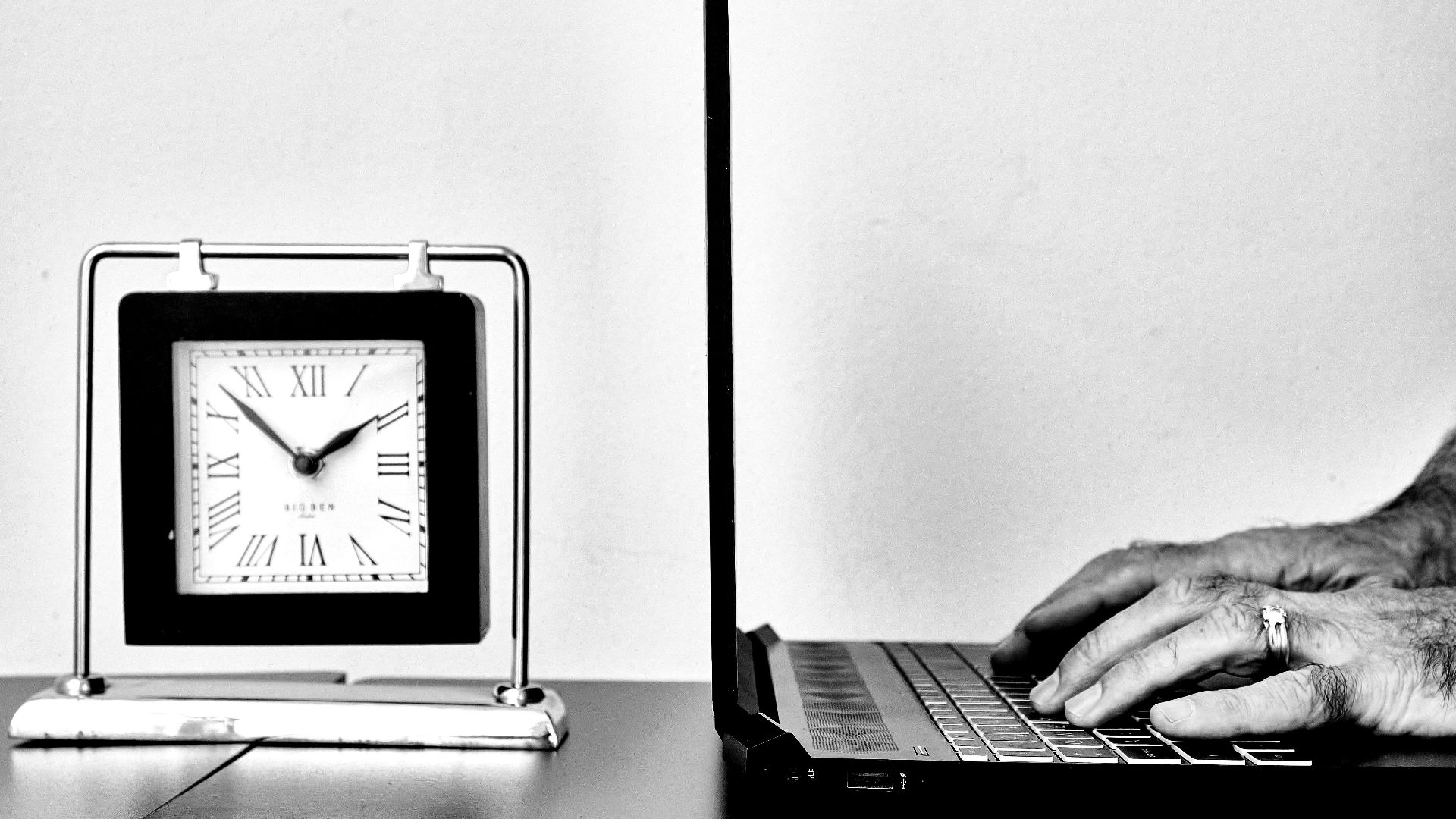 a person typing on a laptop next to a clock