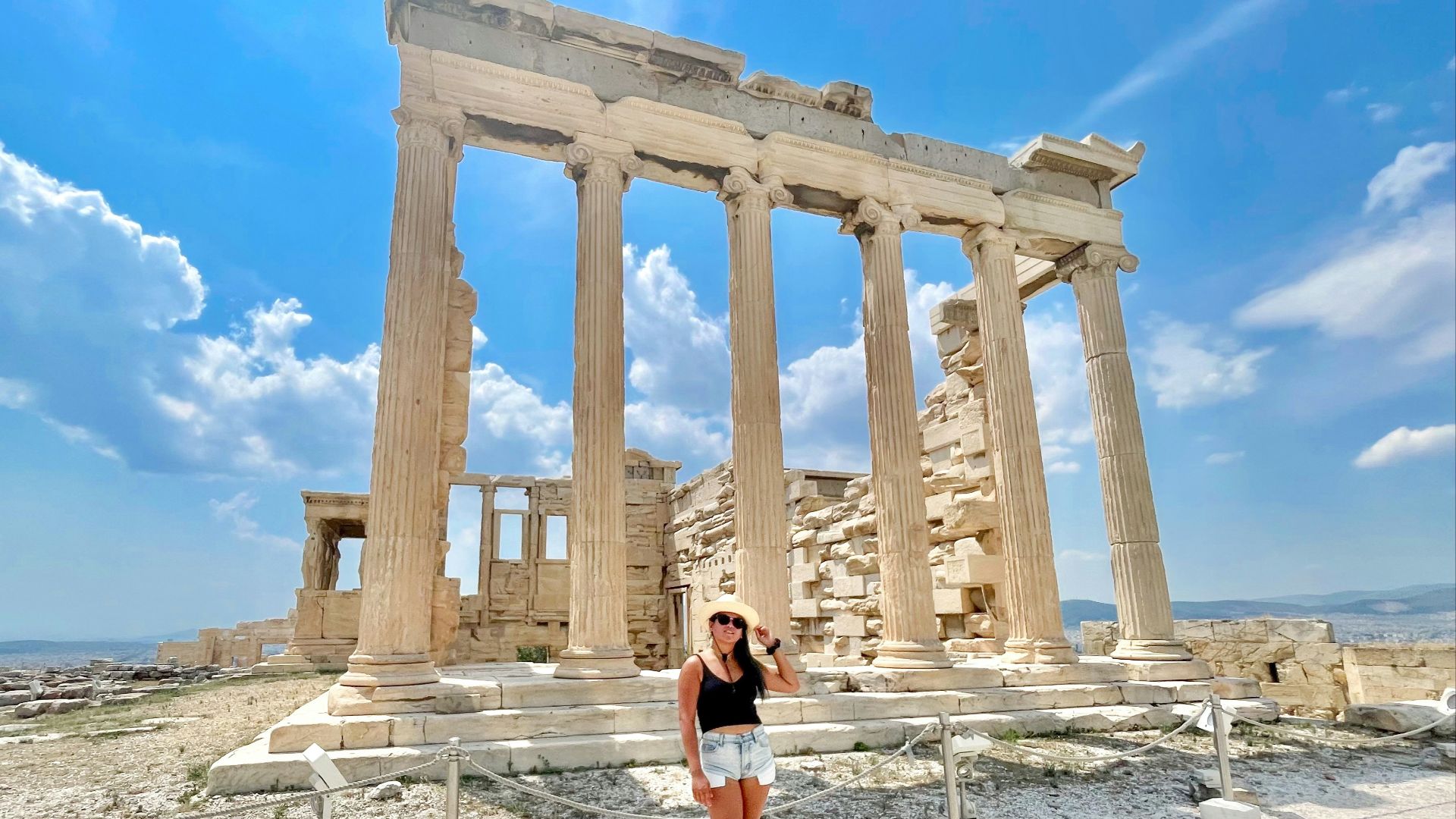 woman in black tank top and blue denim shorts standing near brown concrete building during daytime