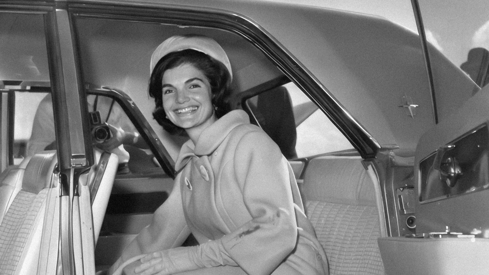 a black and white photo of a woman sitting in a car