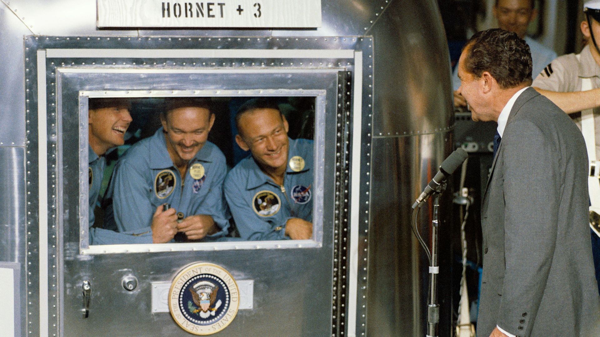 man in gray suit jacket in front of microphone with stand