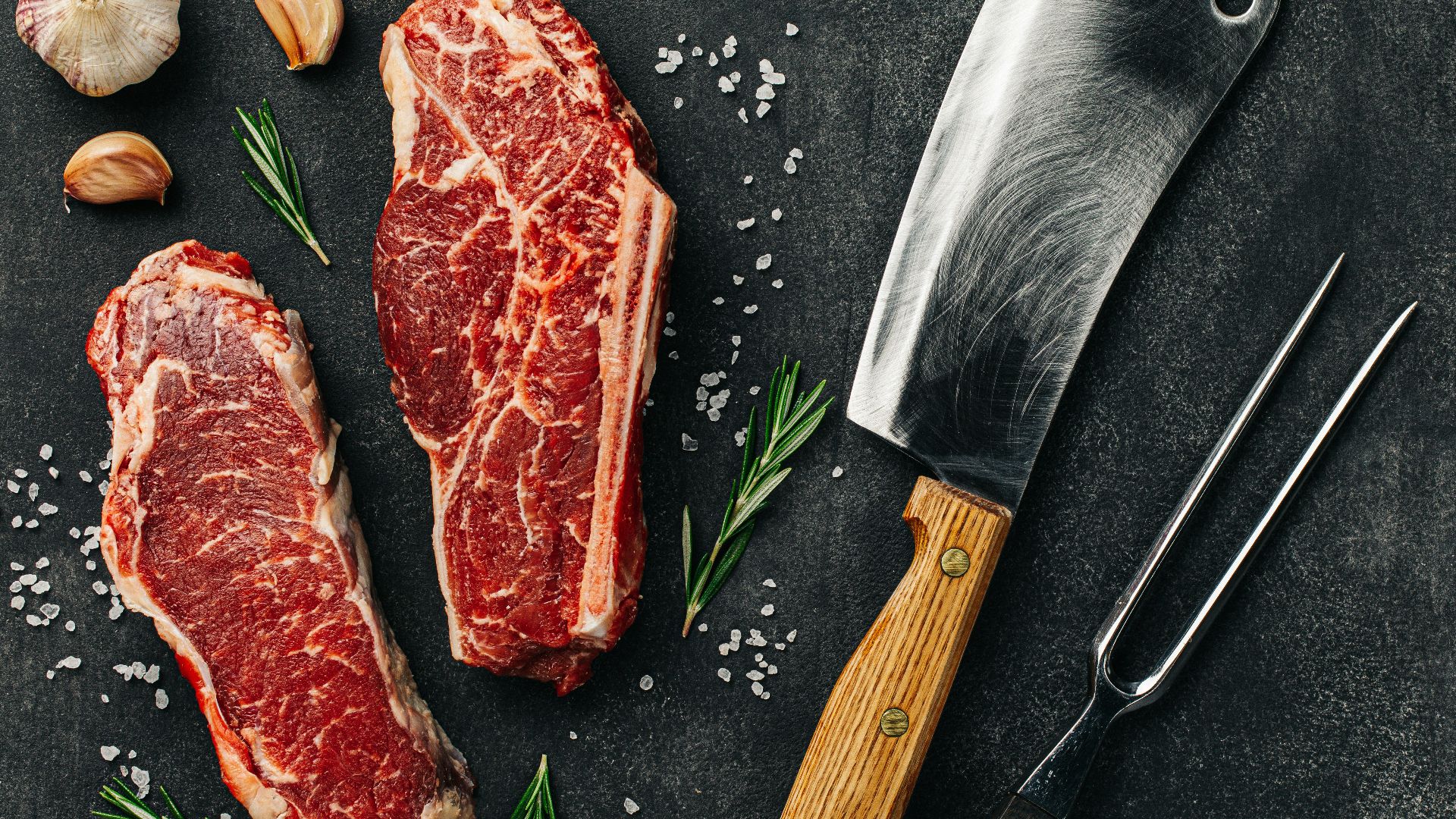 two pieces of raw meat next to a knife and garlic