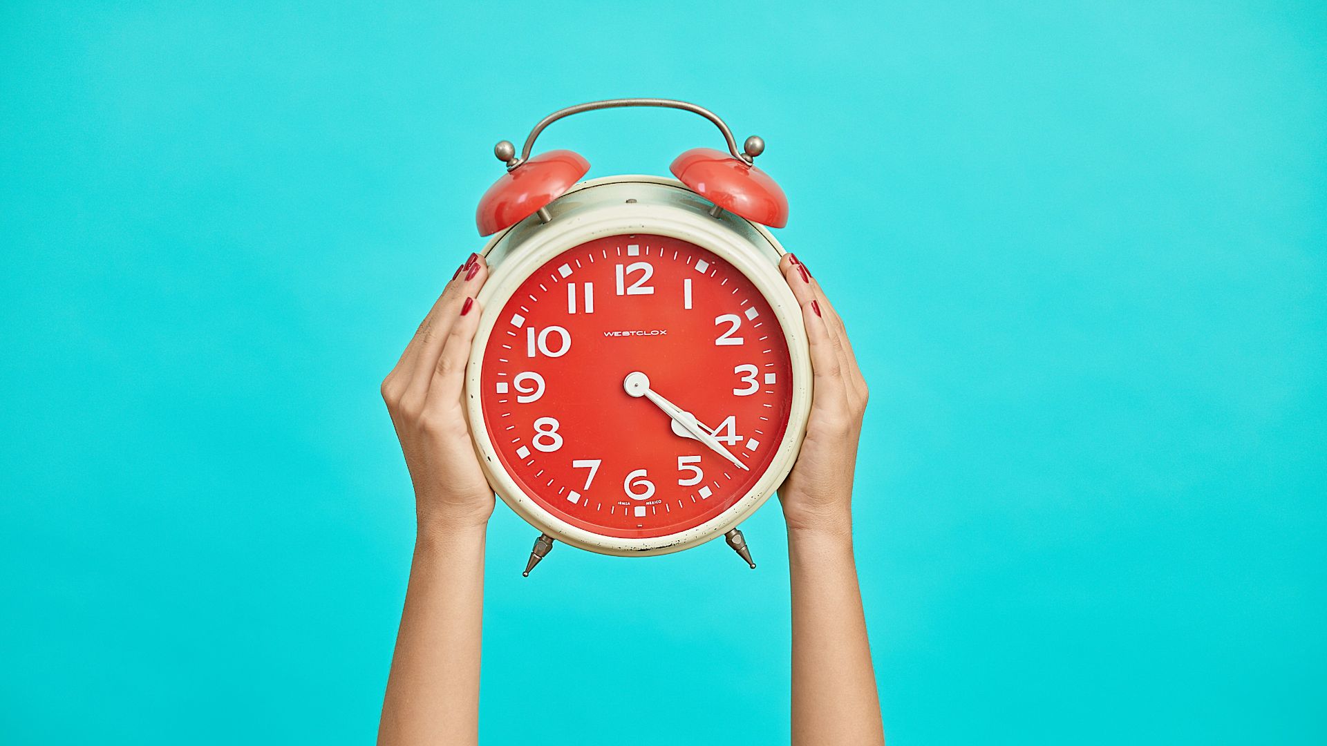 person holding red and beige twin bell analog alarm clock