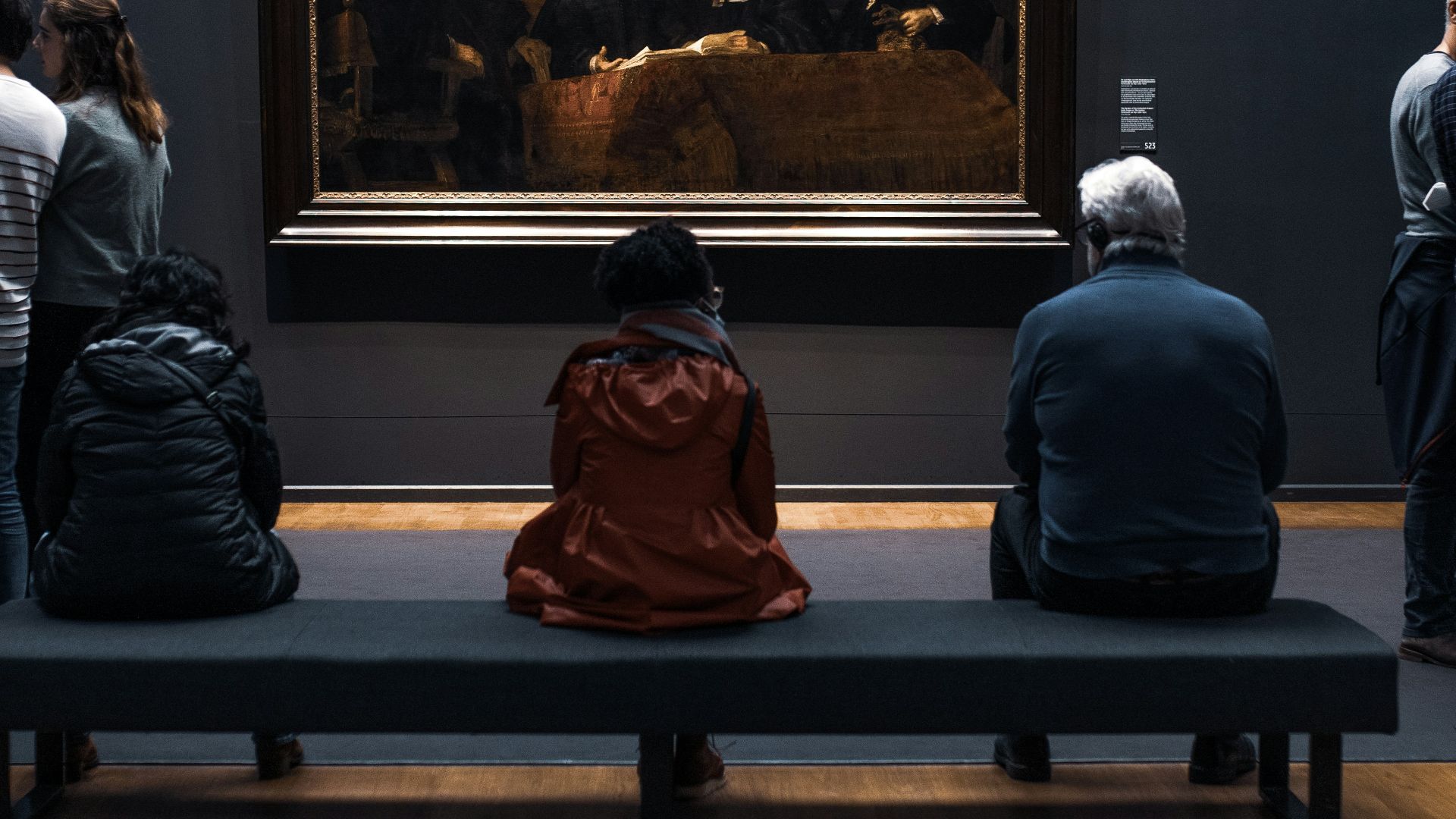 a group of people standing around a museum looking at a painting