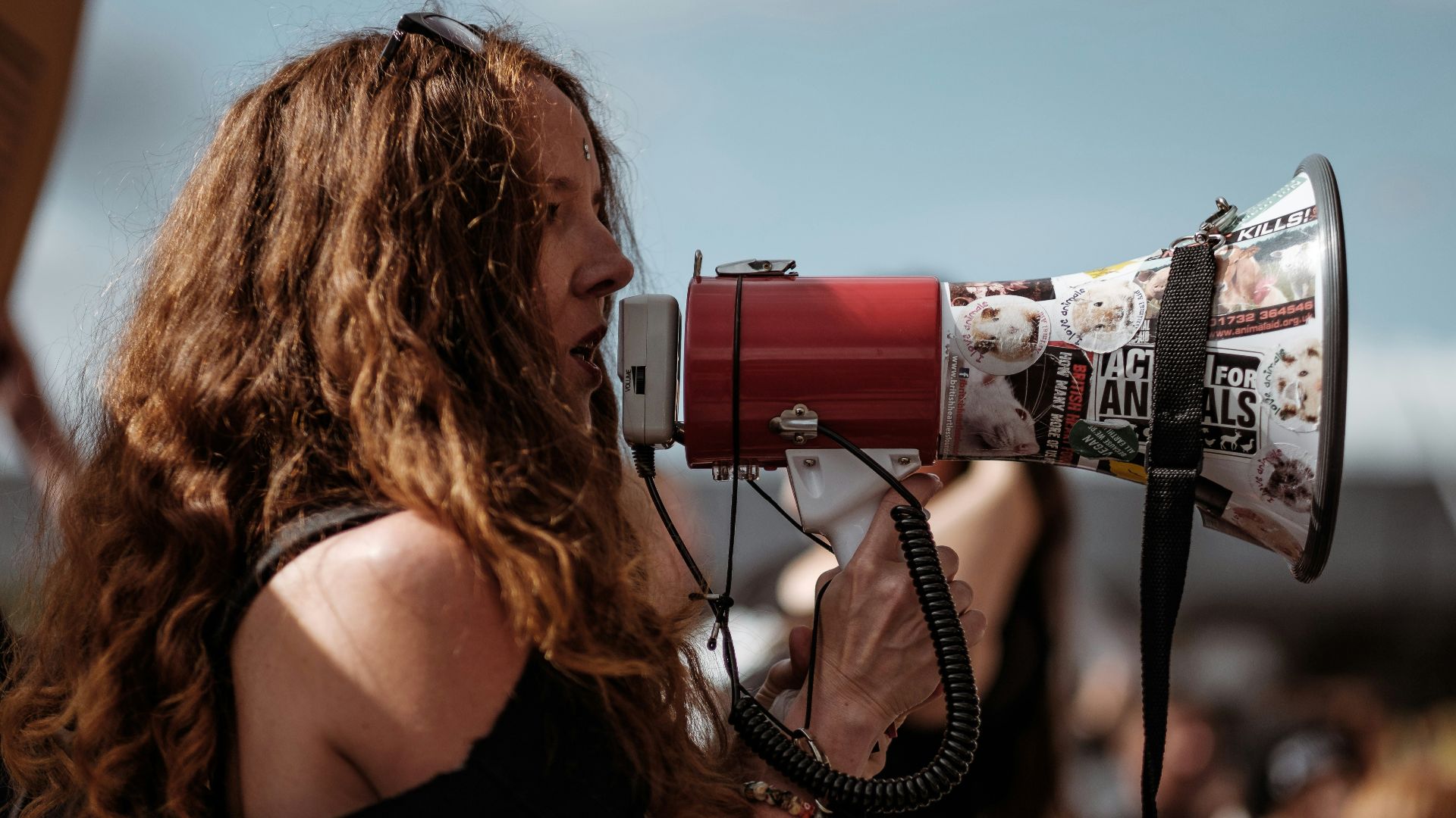 selective focus photography of woman wearing black cold-shoulder shirt using megaphone during daytime