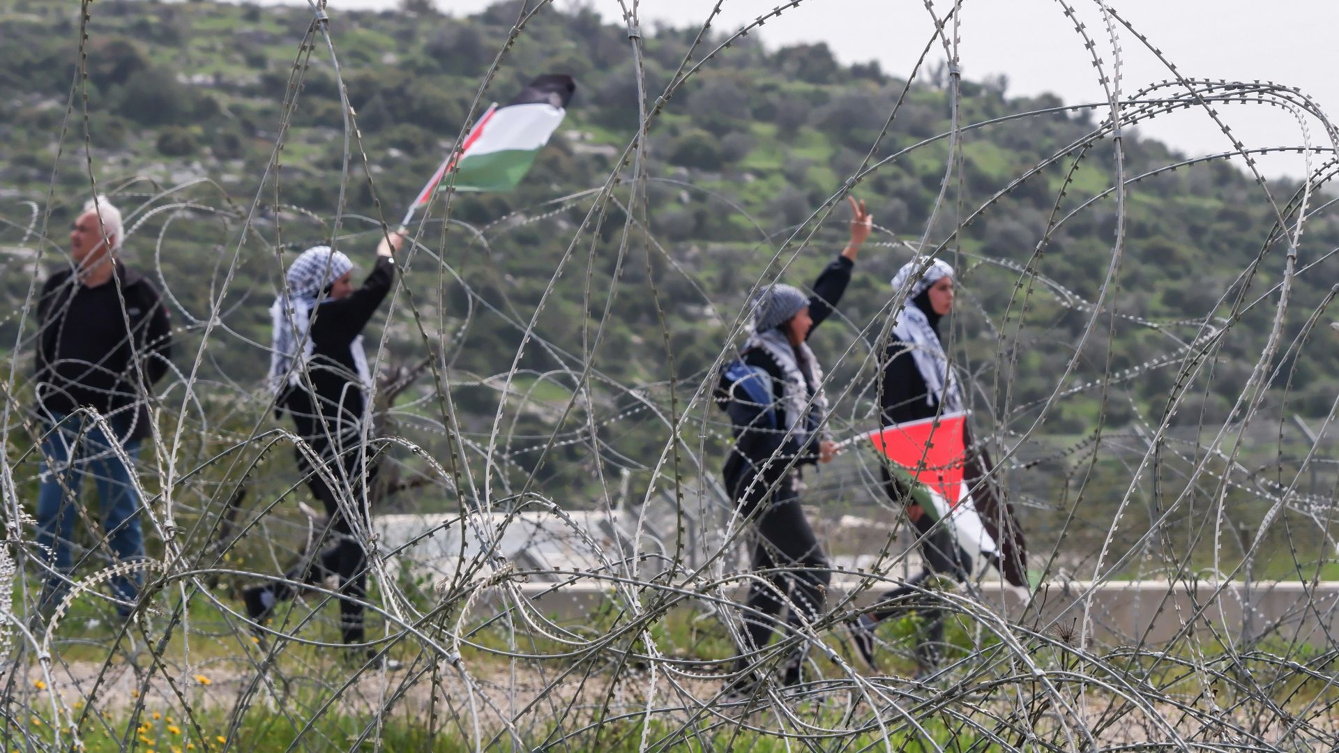 a group of people walking past a barbed wire fence