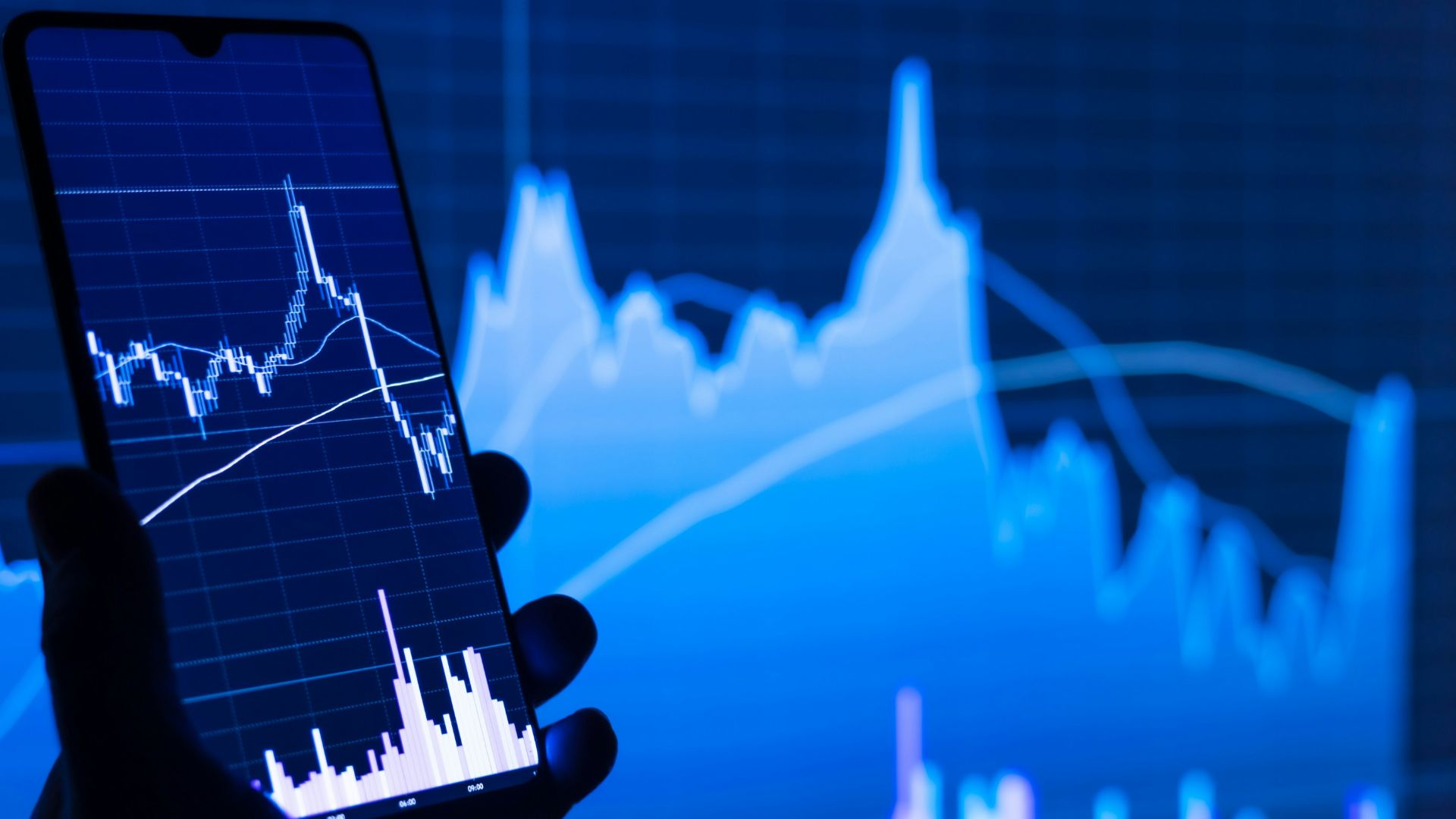 a person holding a cell phone in front of a stock chart