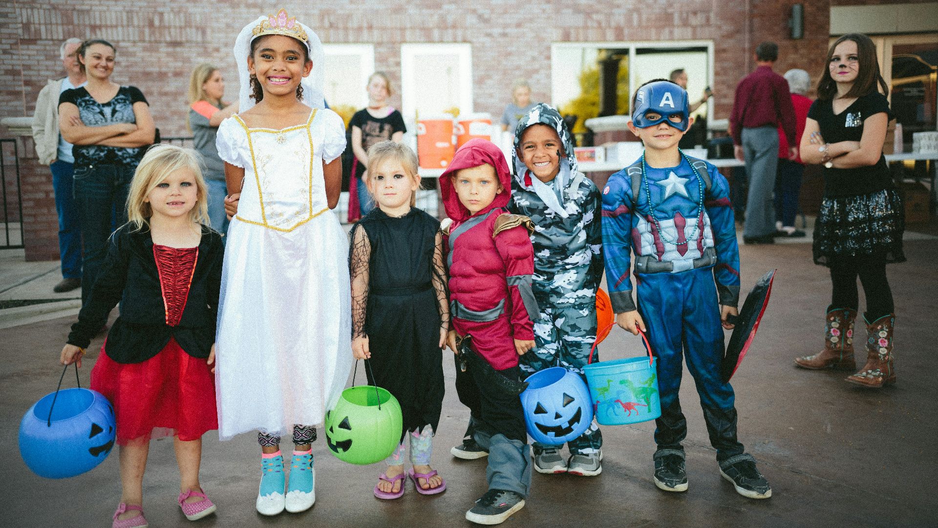 children standing while holding Jack 'o lantern and wearing costume