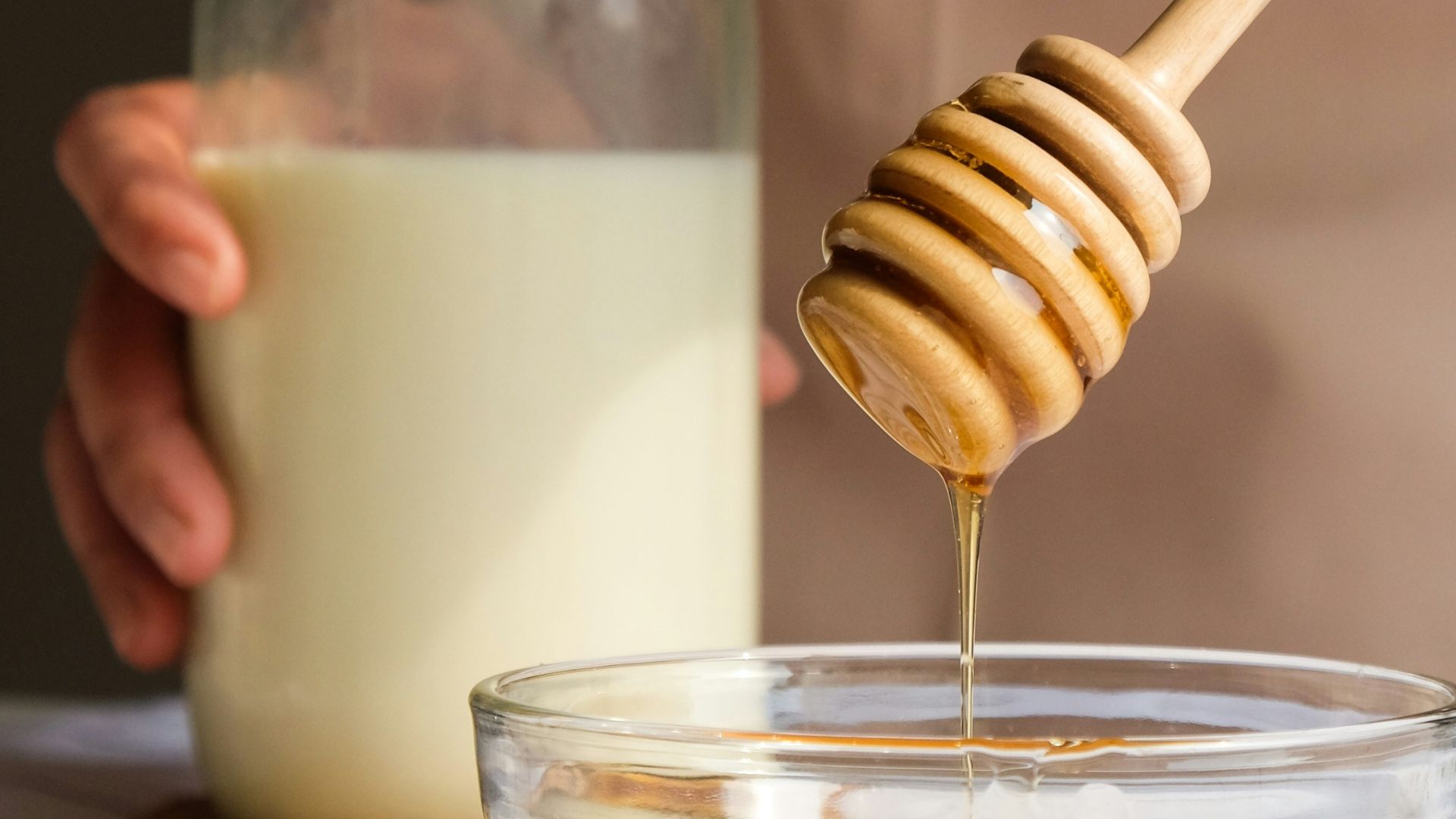 person holding clear glass jar with white liquid