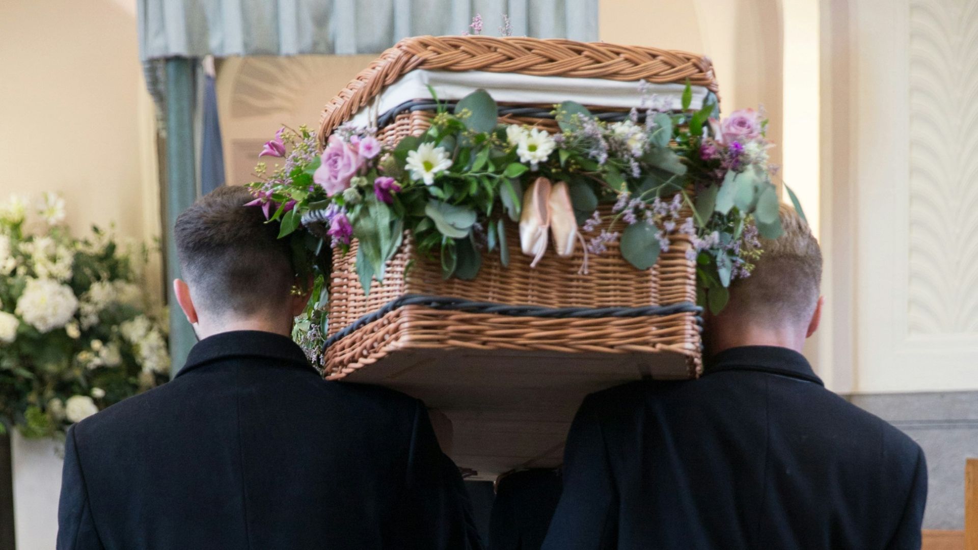 two men carrying a casket with flowers on it