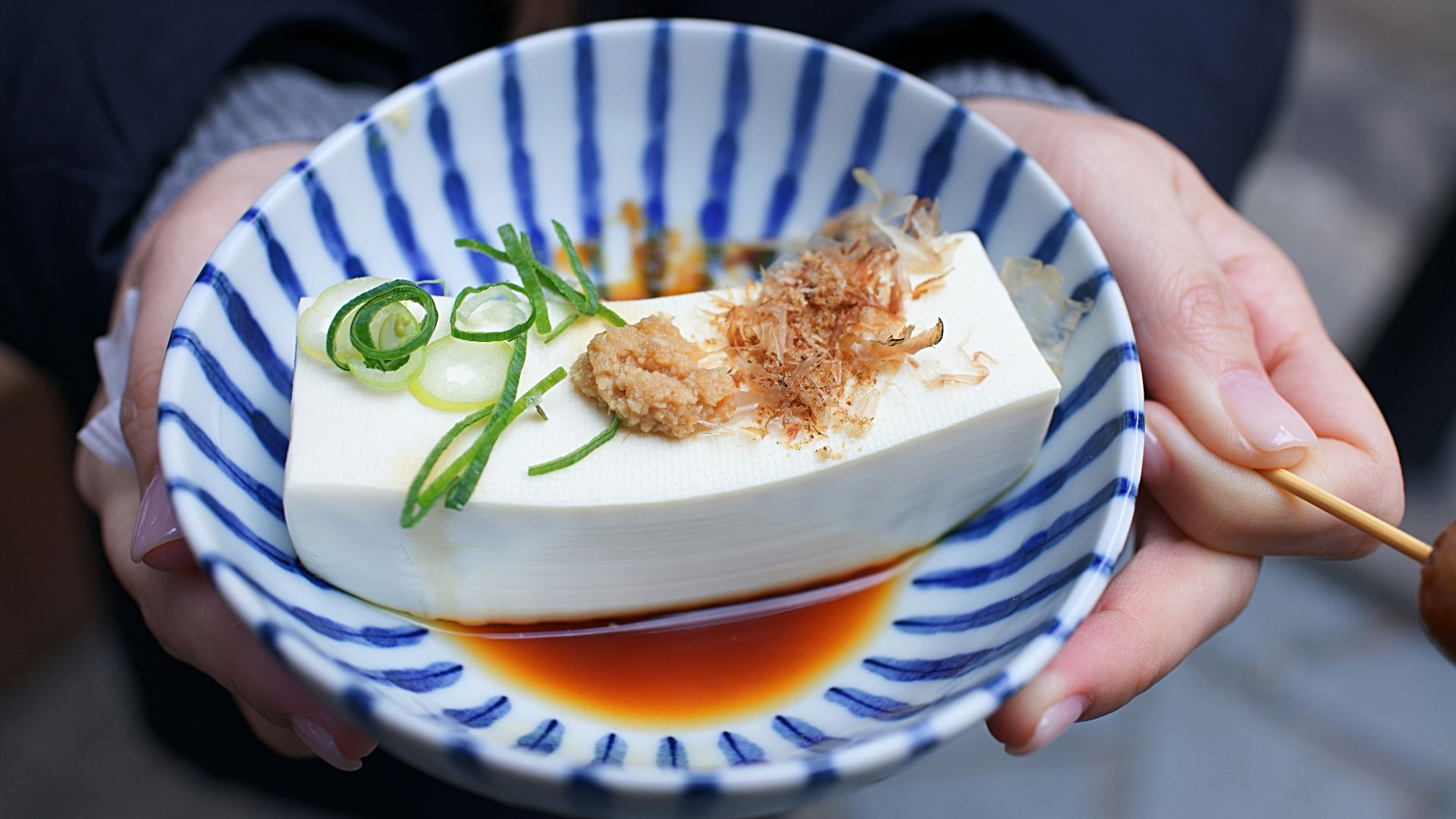 person holding white and blue ceramic plate with rice and sliced cucumber
