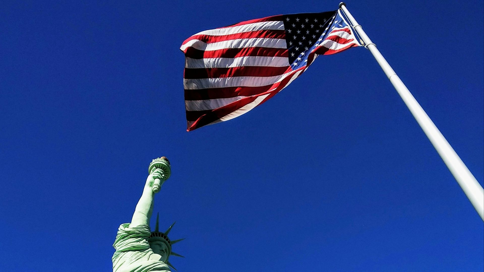Statue of Liberty in front USA flag under blue sky