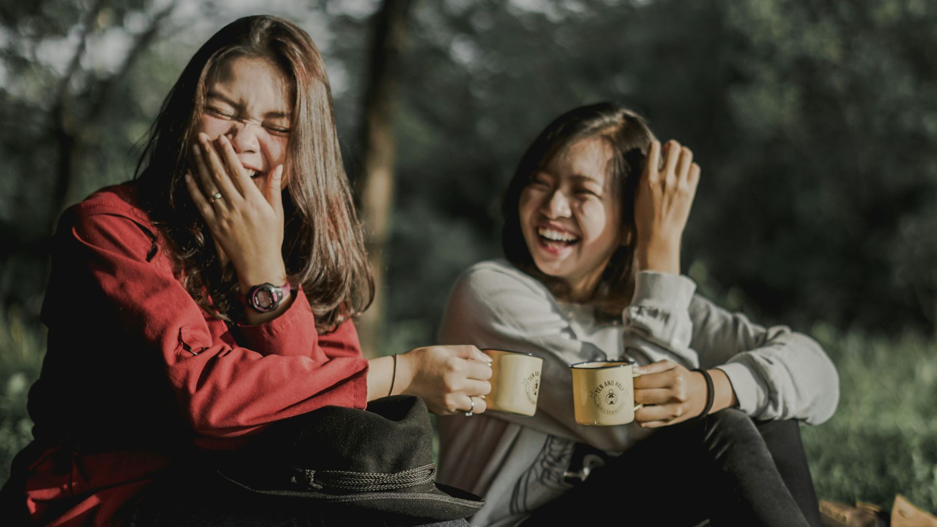 two women holding cups laughing at each other