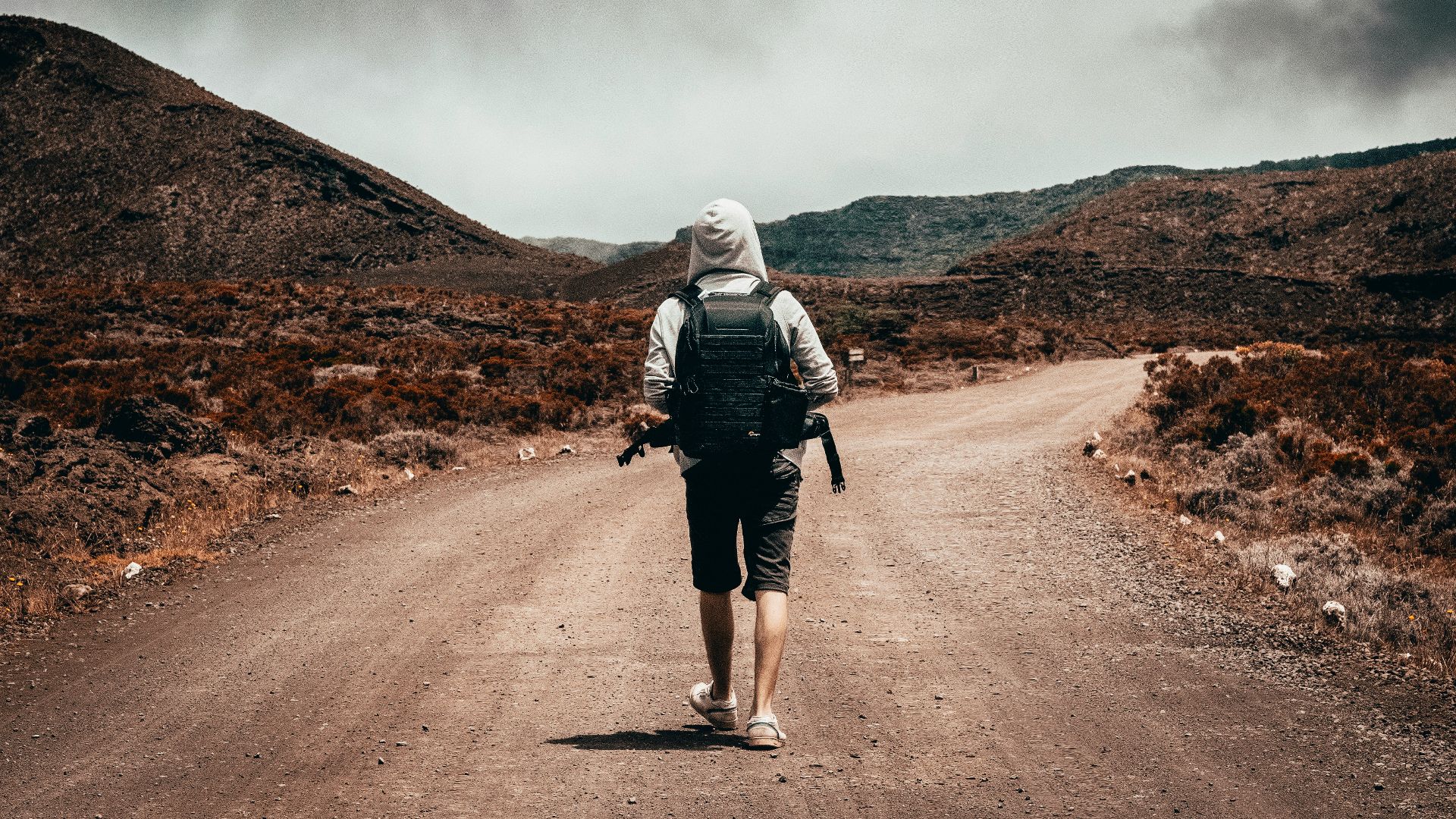 man in gray hoodie carrying backpack walking under the sun