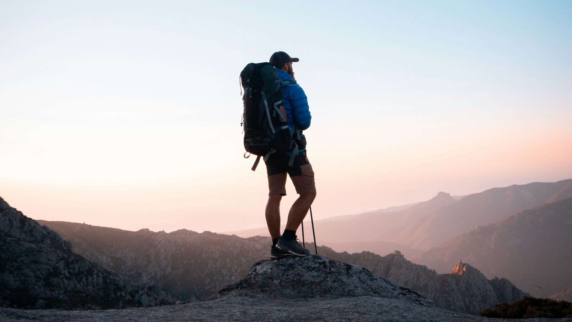man in black jacket and blue denim shorts with black hiking backpack standing on mountain during