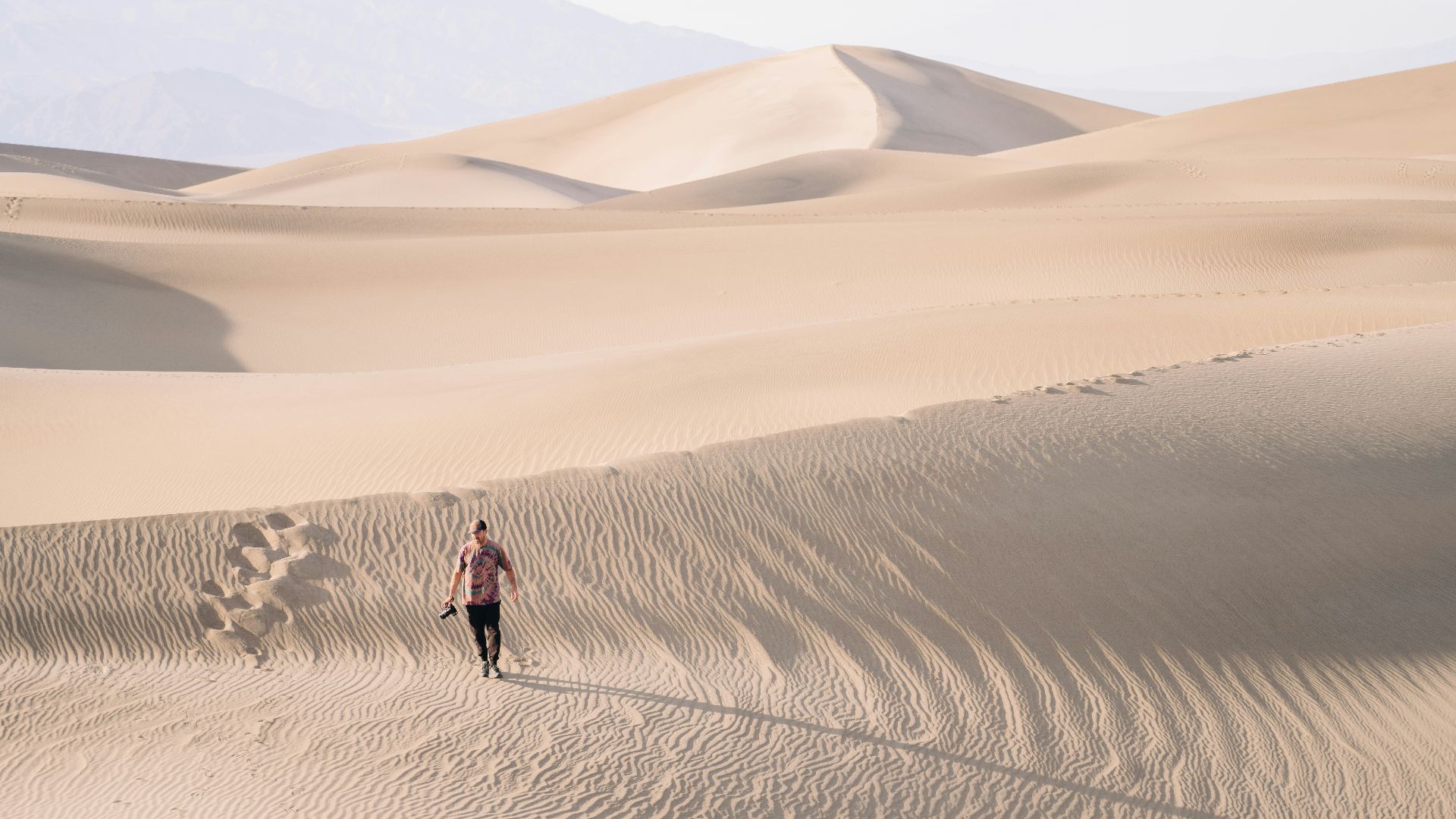 a man walking across a sandy desert with mountains in the background