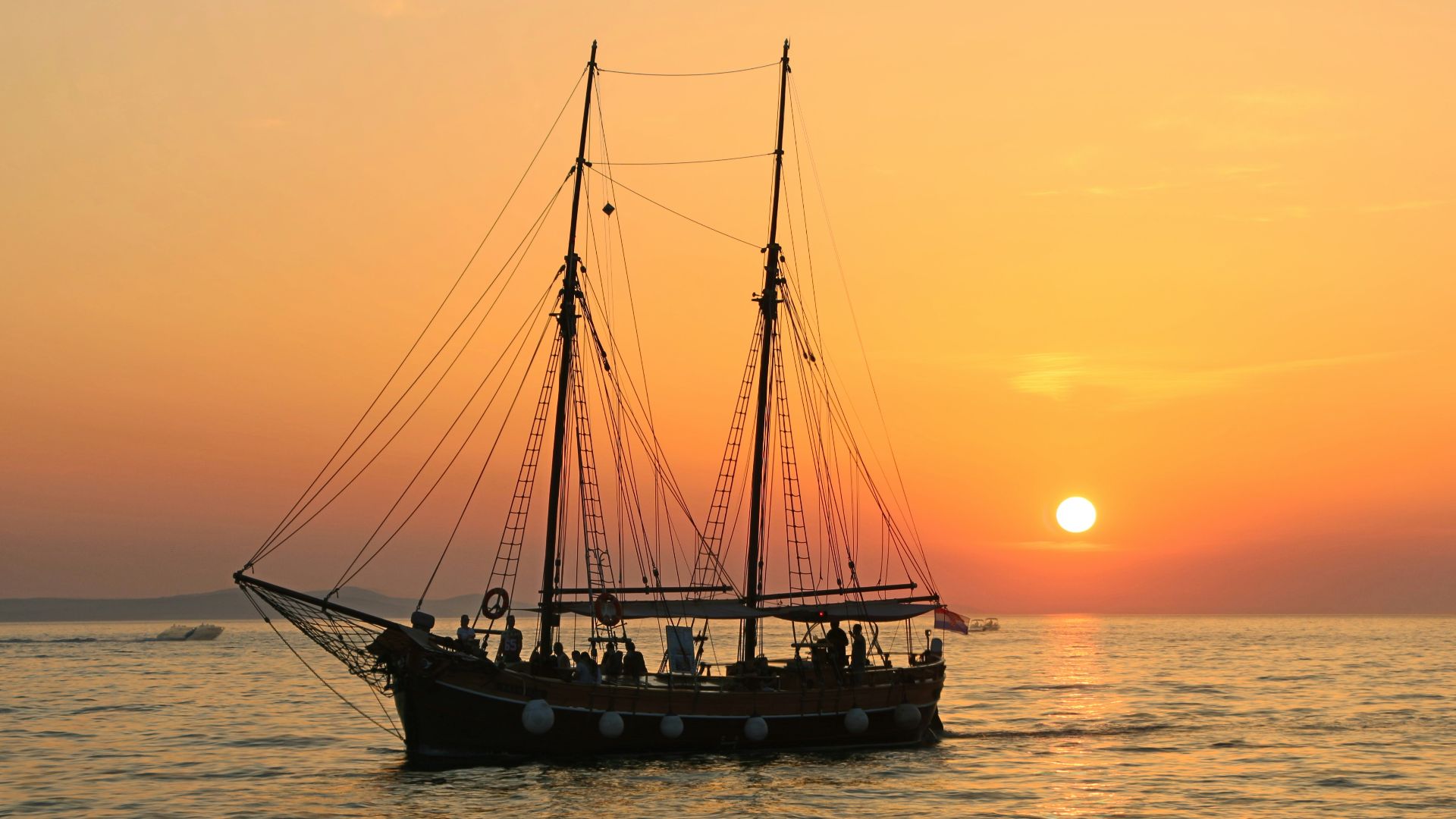 black and white sailboat in body of water during sunset