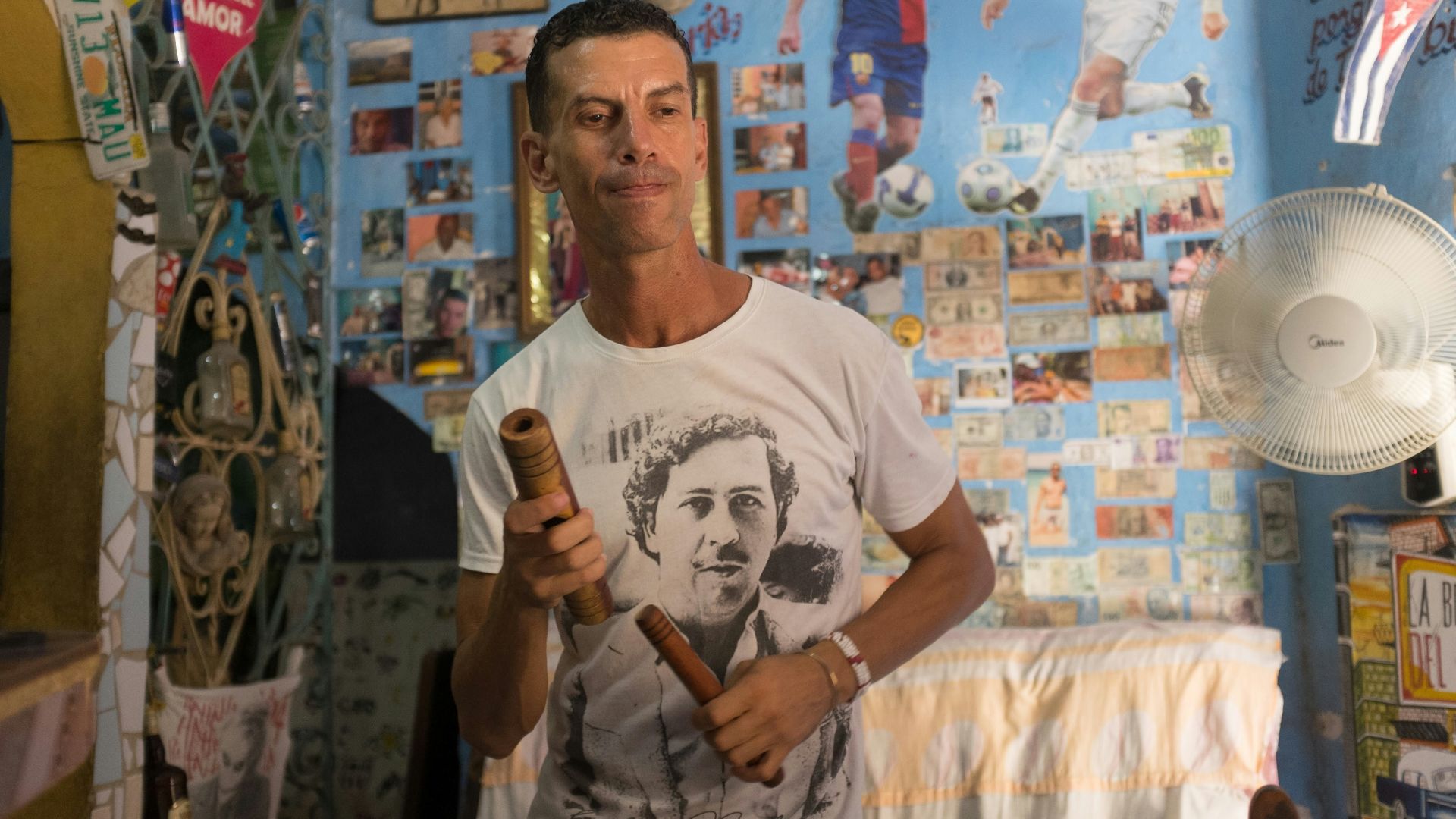A man holding a bottle in a room with pictures on the wall