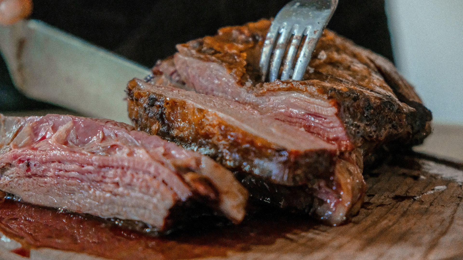 person slicing a meat on brown wooden board