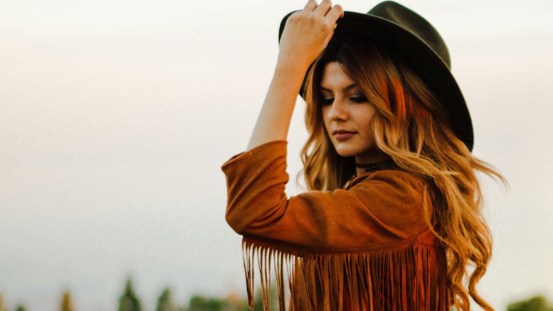 woman wearing brown jacket with fringe holding hat during daytime