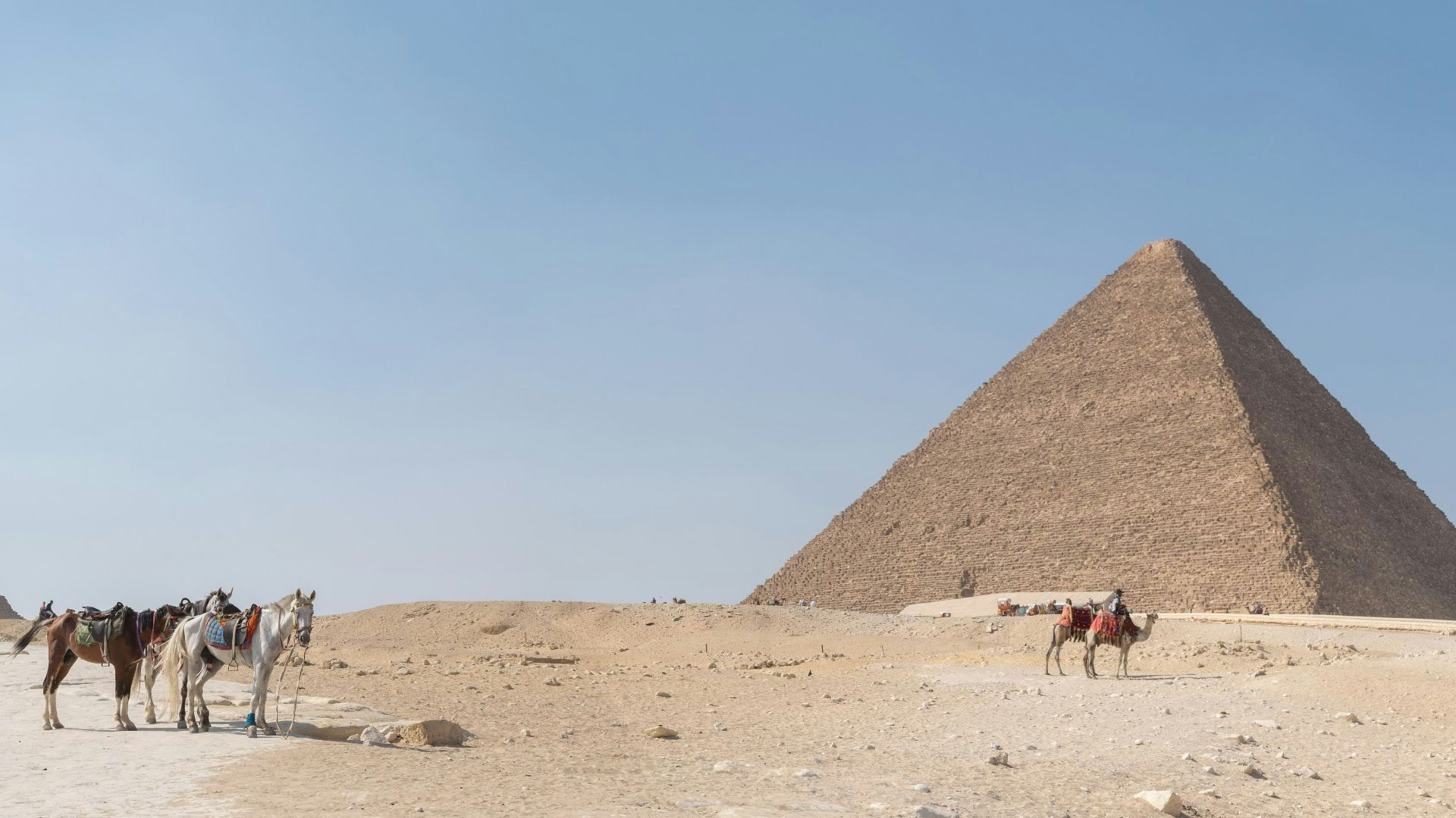a group of people riding horses in front of three pyramids