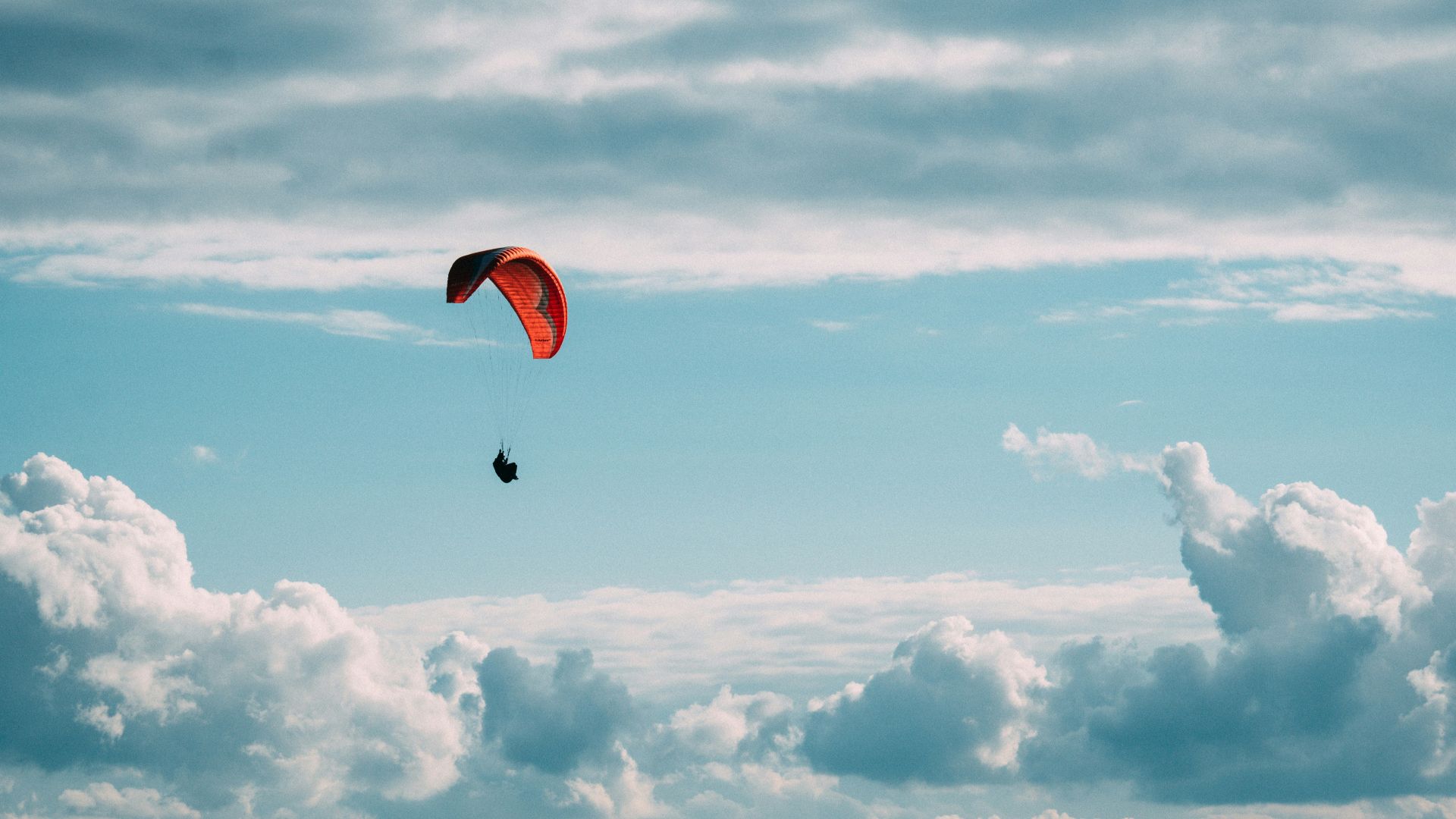 person in red parachute under white clouds during daytime