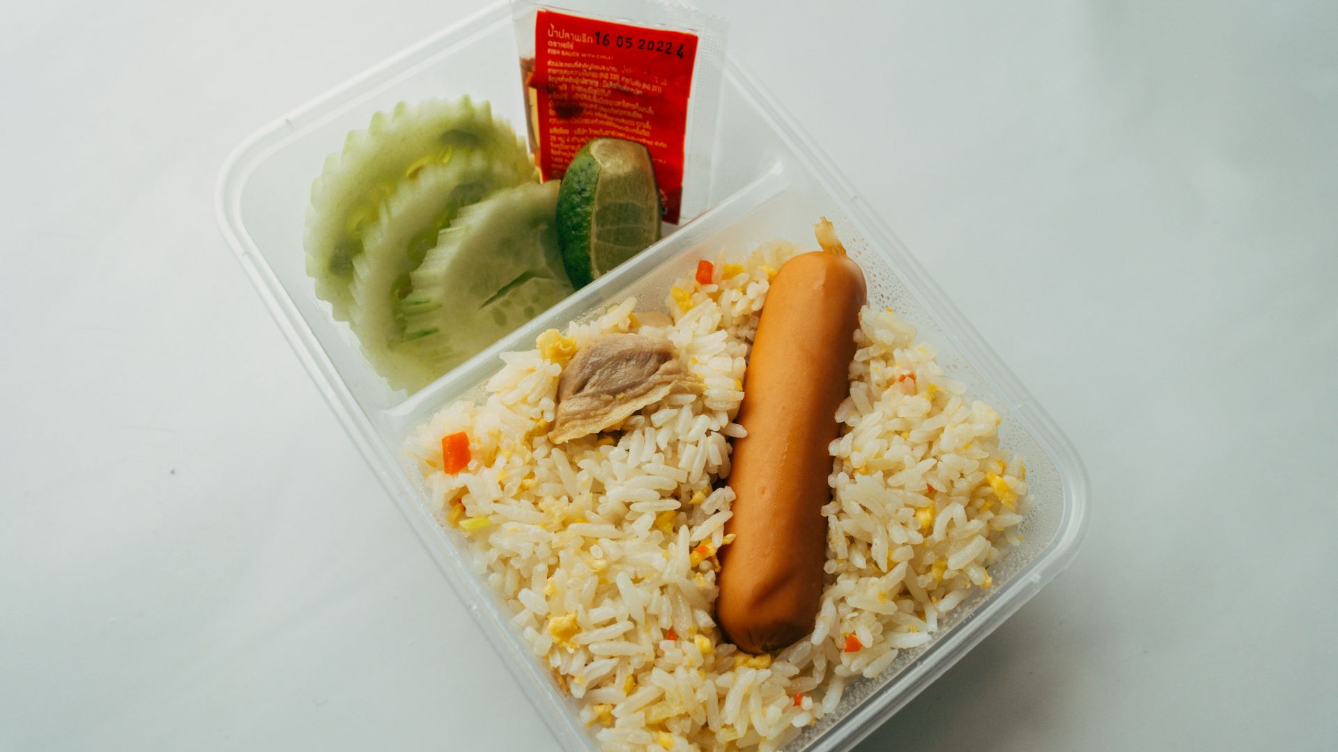 a plastic container filled with rice and a hot dog