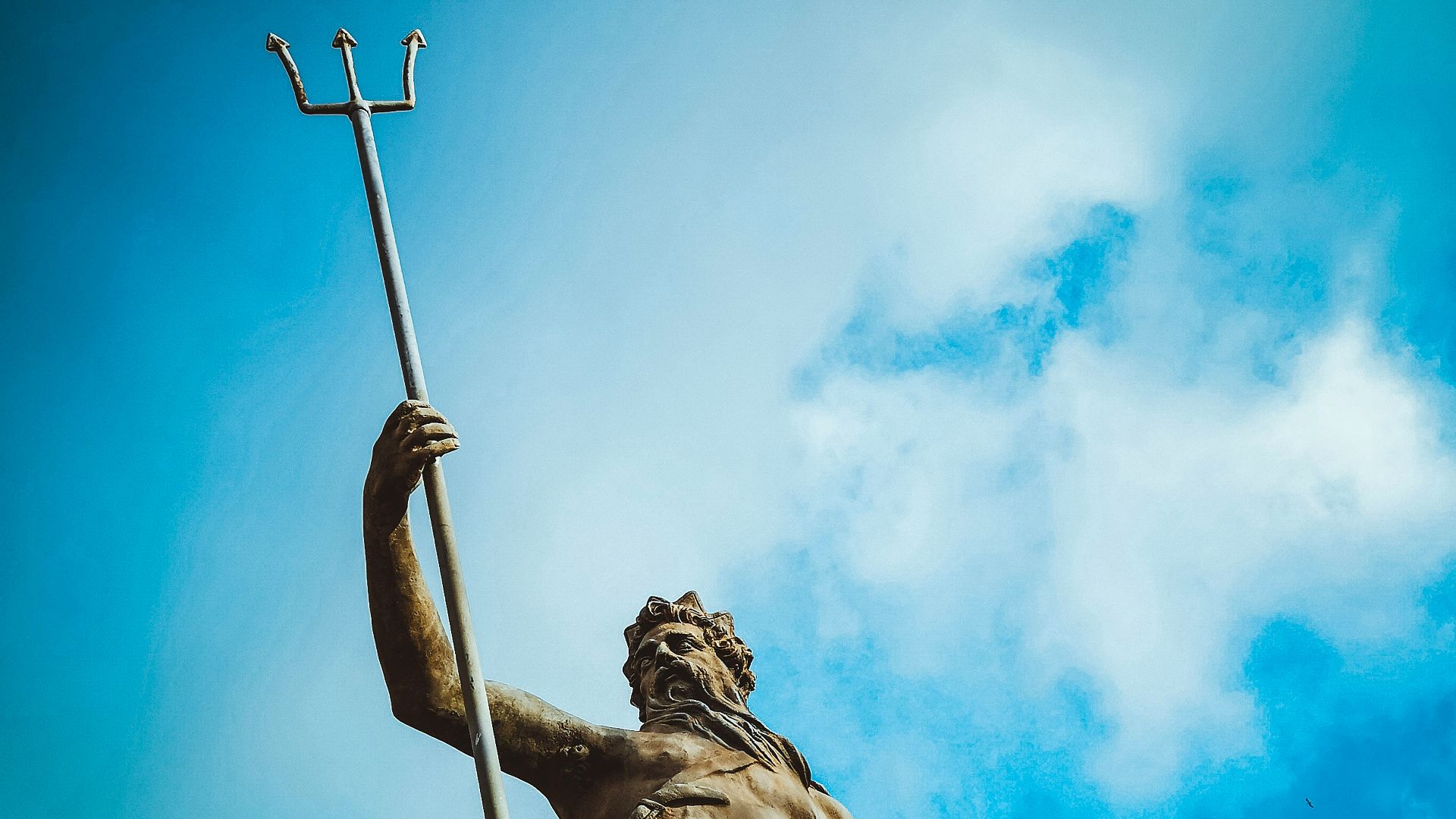 man holding trident statue under white clouds at daytime