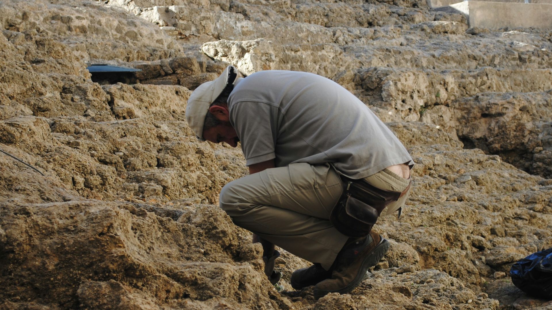 man in gray jacket and brown pants sitting on brown rock during daytime