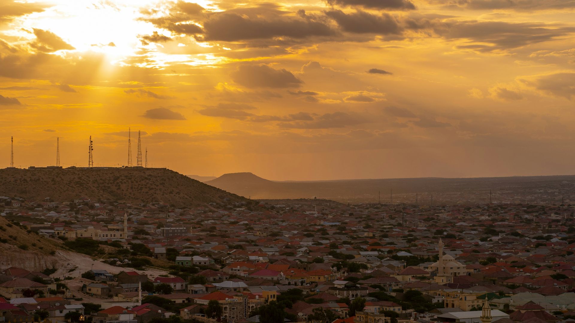 The sun is setting over a city and hills