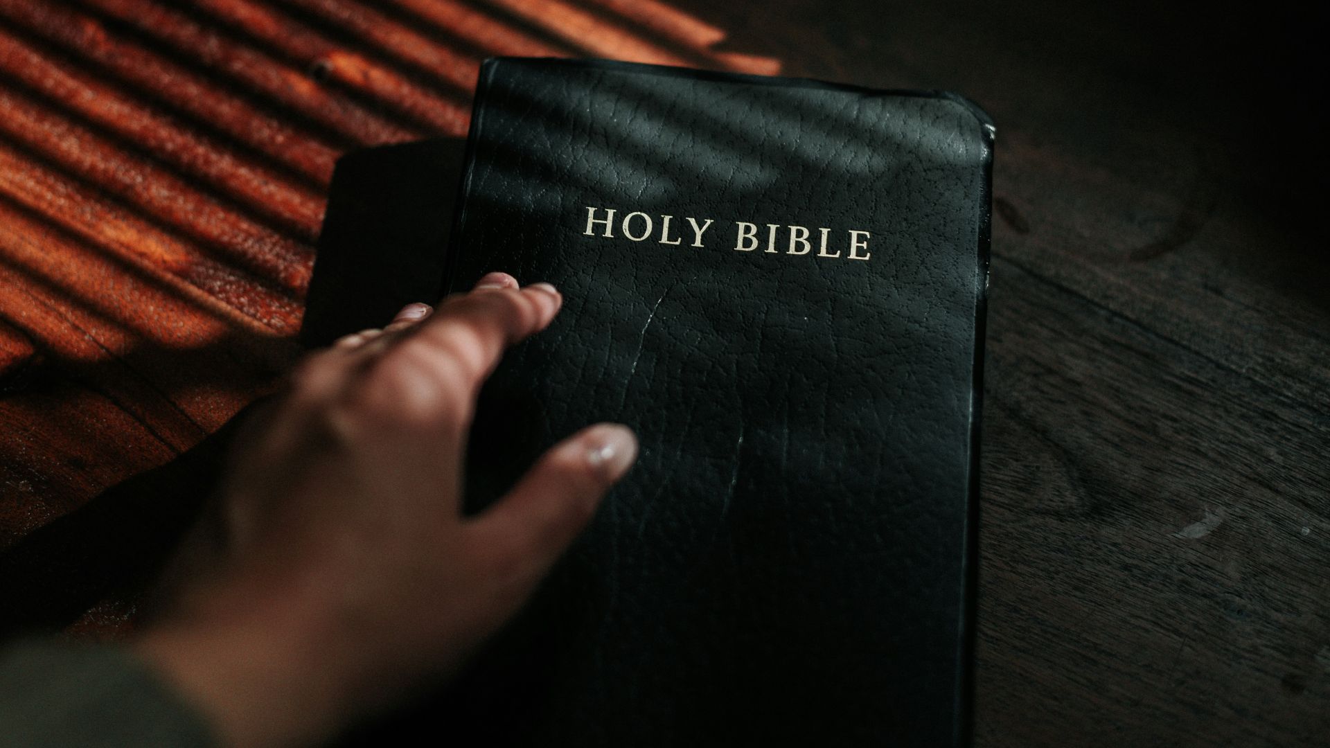 person holding black book on brown wooden surface