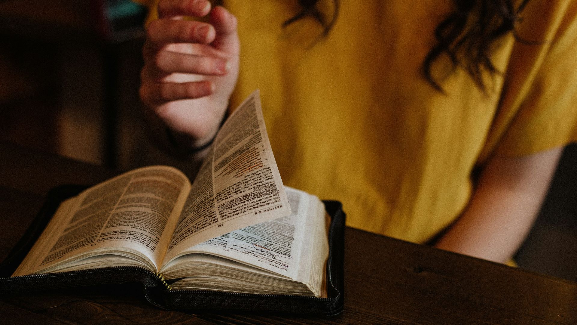 person reading Bible on top of brown wooden table