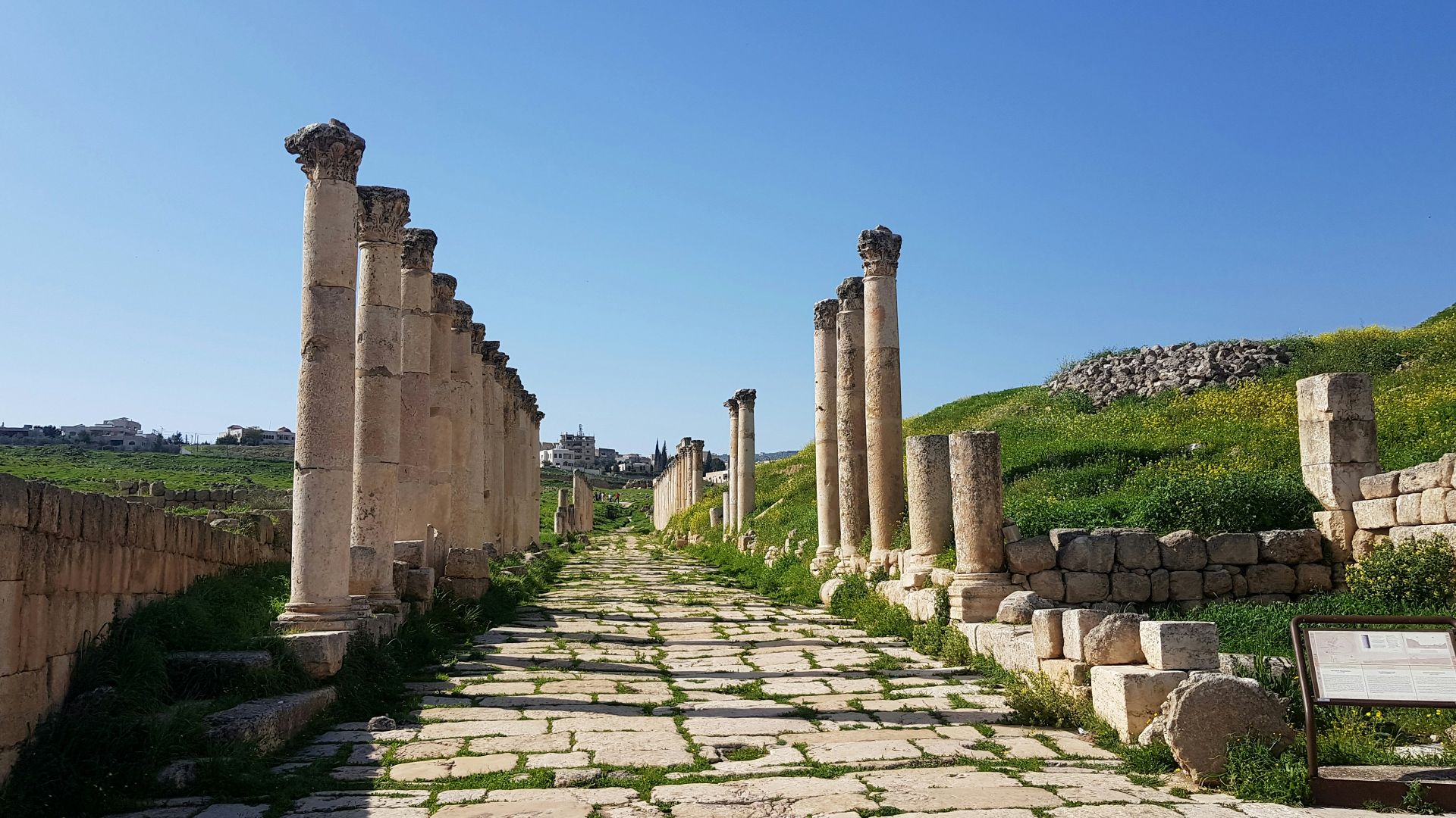 a stone path lined with columns and a sign