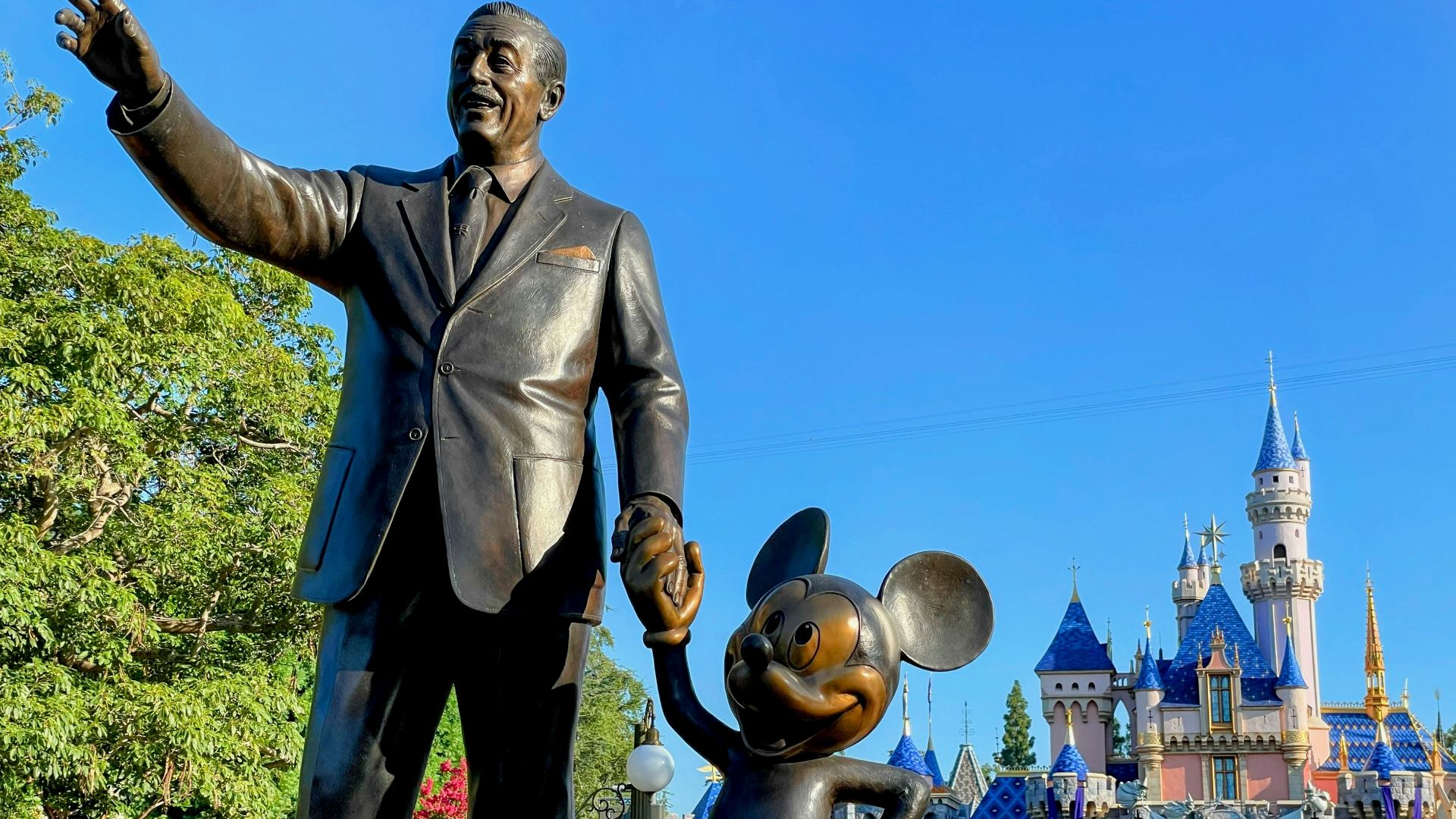 a statue of walt and mickey mouse in front of a castle