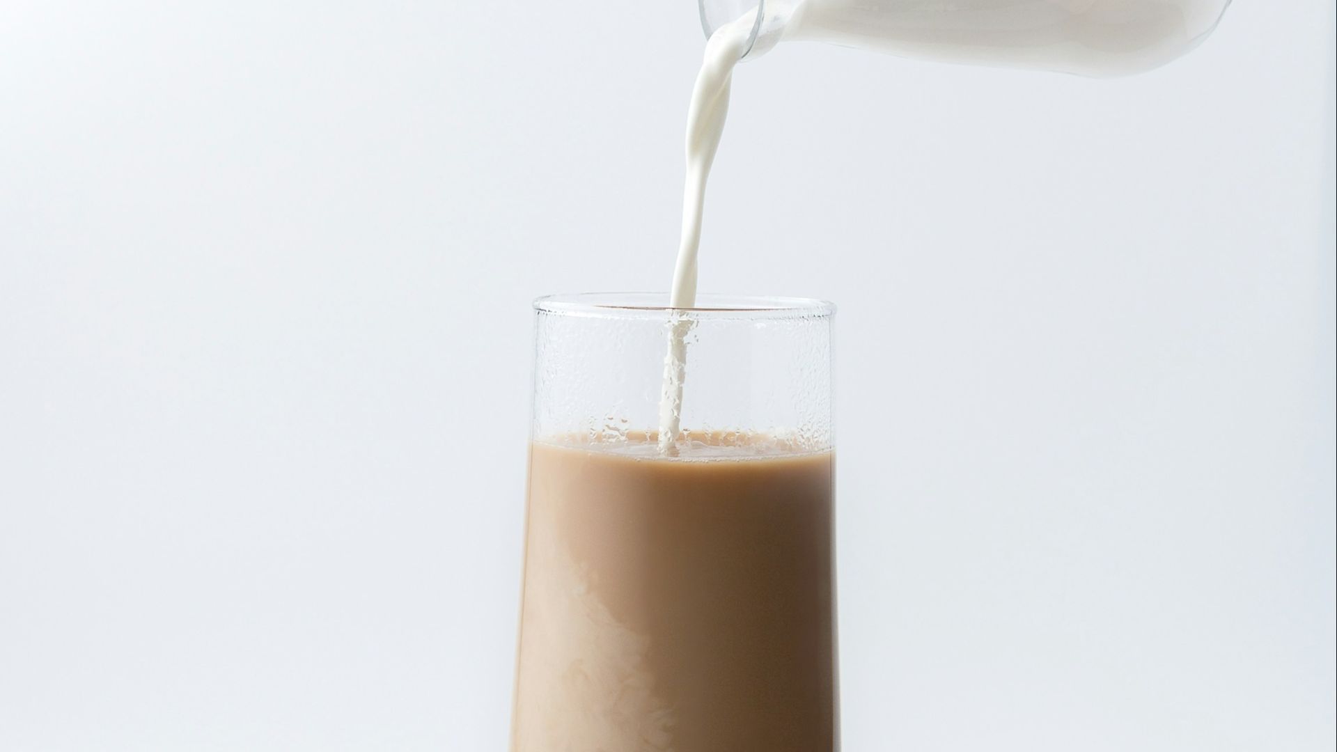 person pouring milk into chocolate filled glass cup