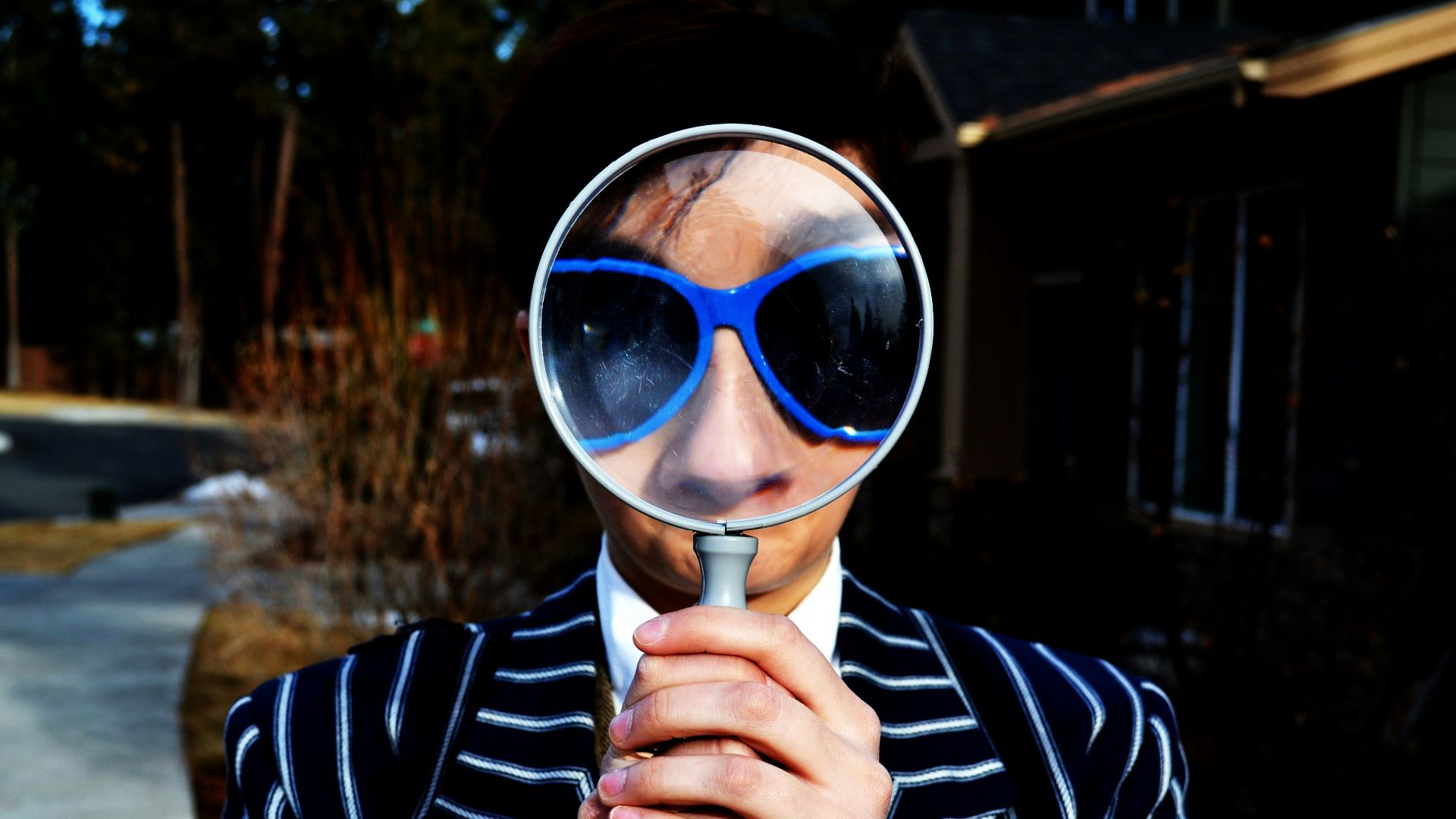 person using magnifying glass enlarging the appearance of his nose and sunglasses
