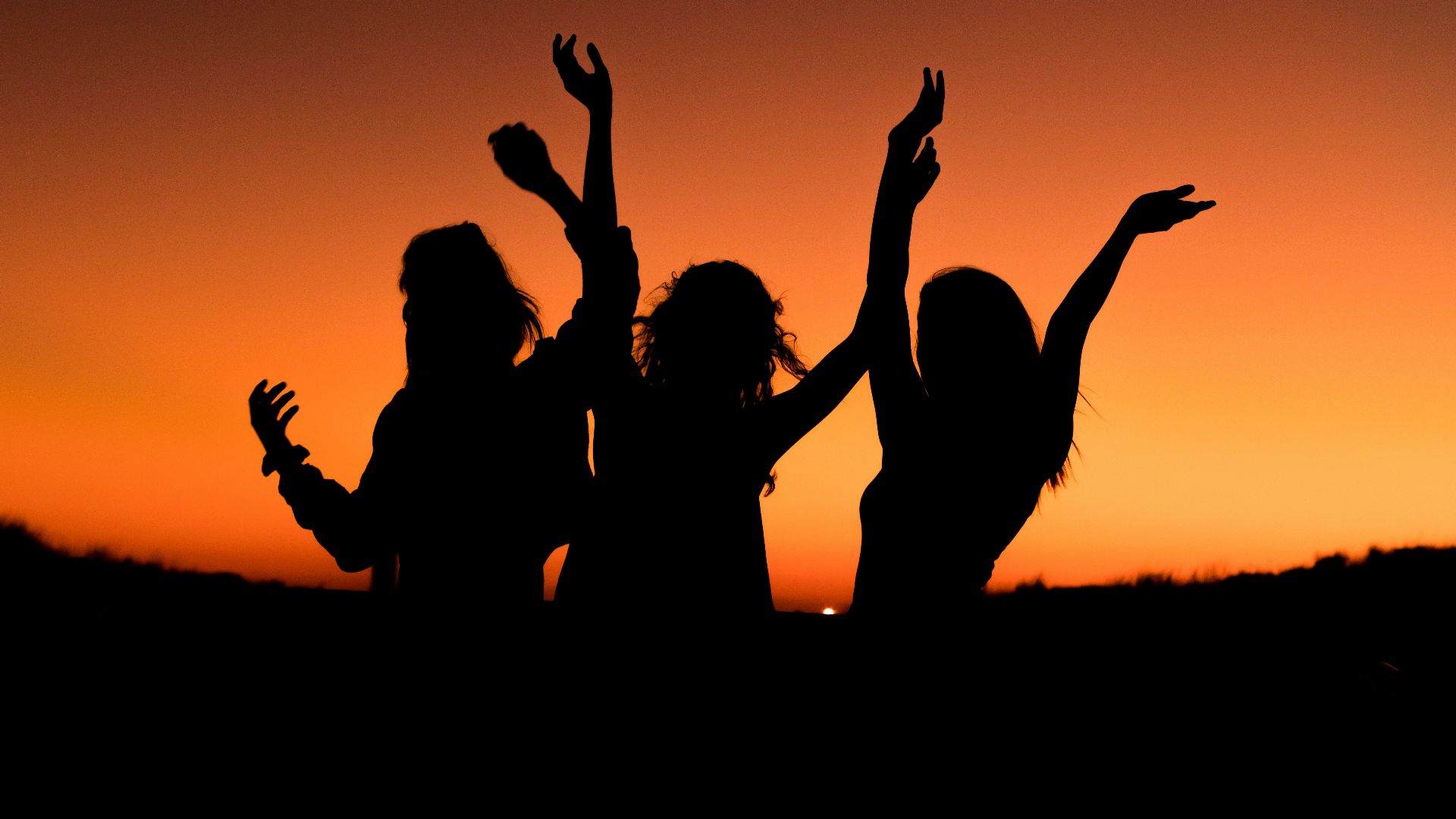 silhouette of three woman with hands on the air while dancing during sunset