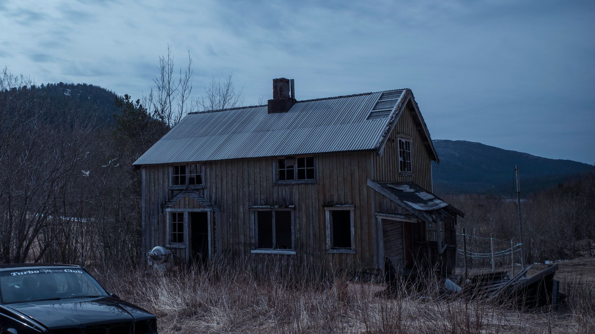 black car parked beside brown wooden house during daytime