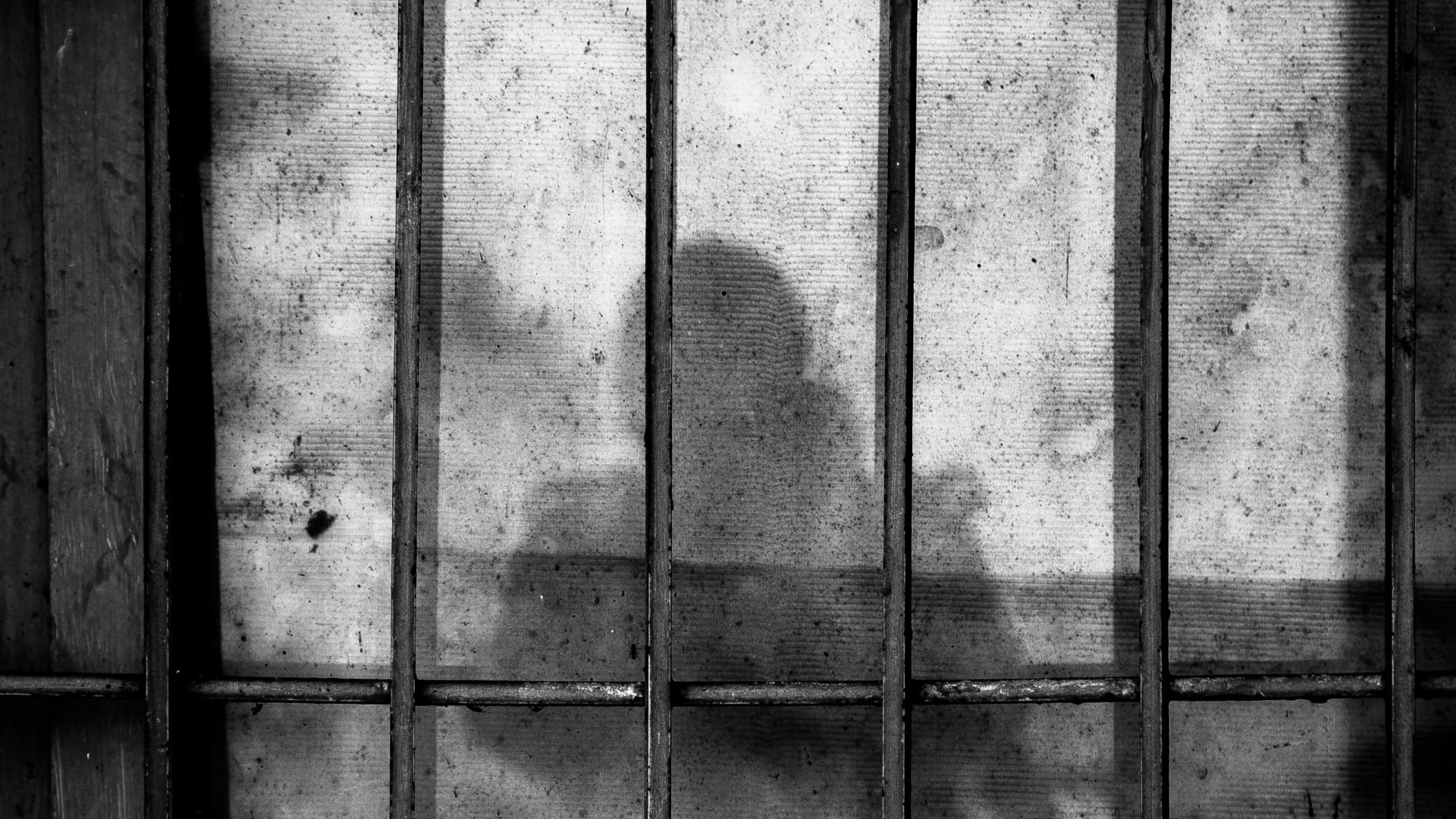 a shadow of a person behind bars in a jail cell