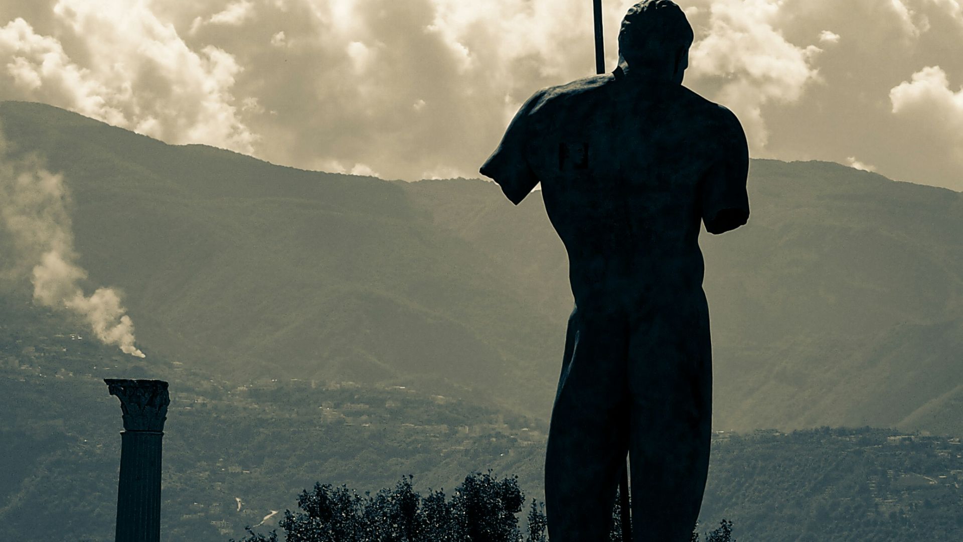 silhouette of man standing on concrete wall near mountain under cloudy sky during daytime