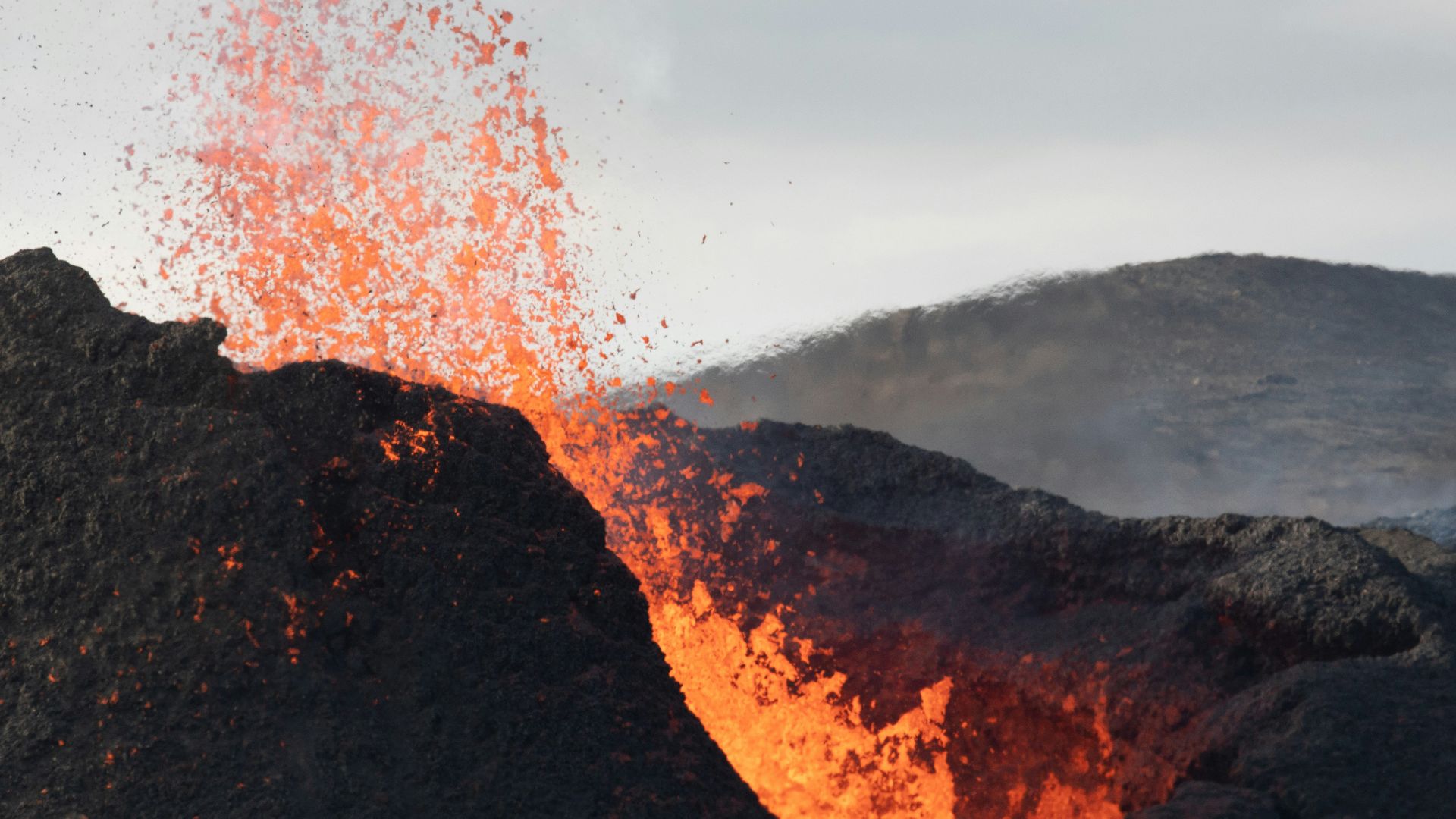 fire on brown rocky mountain under gray sky