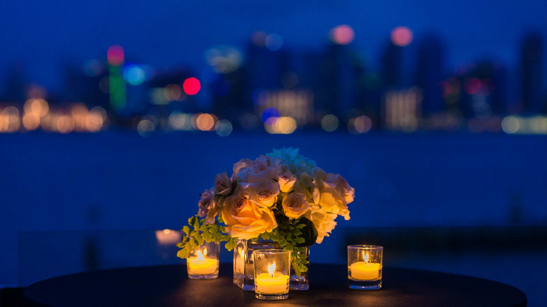 white rose bouquet in vase with three tealight candle votives on round brown wooden table