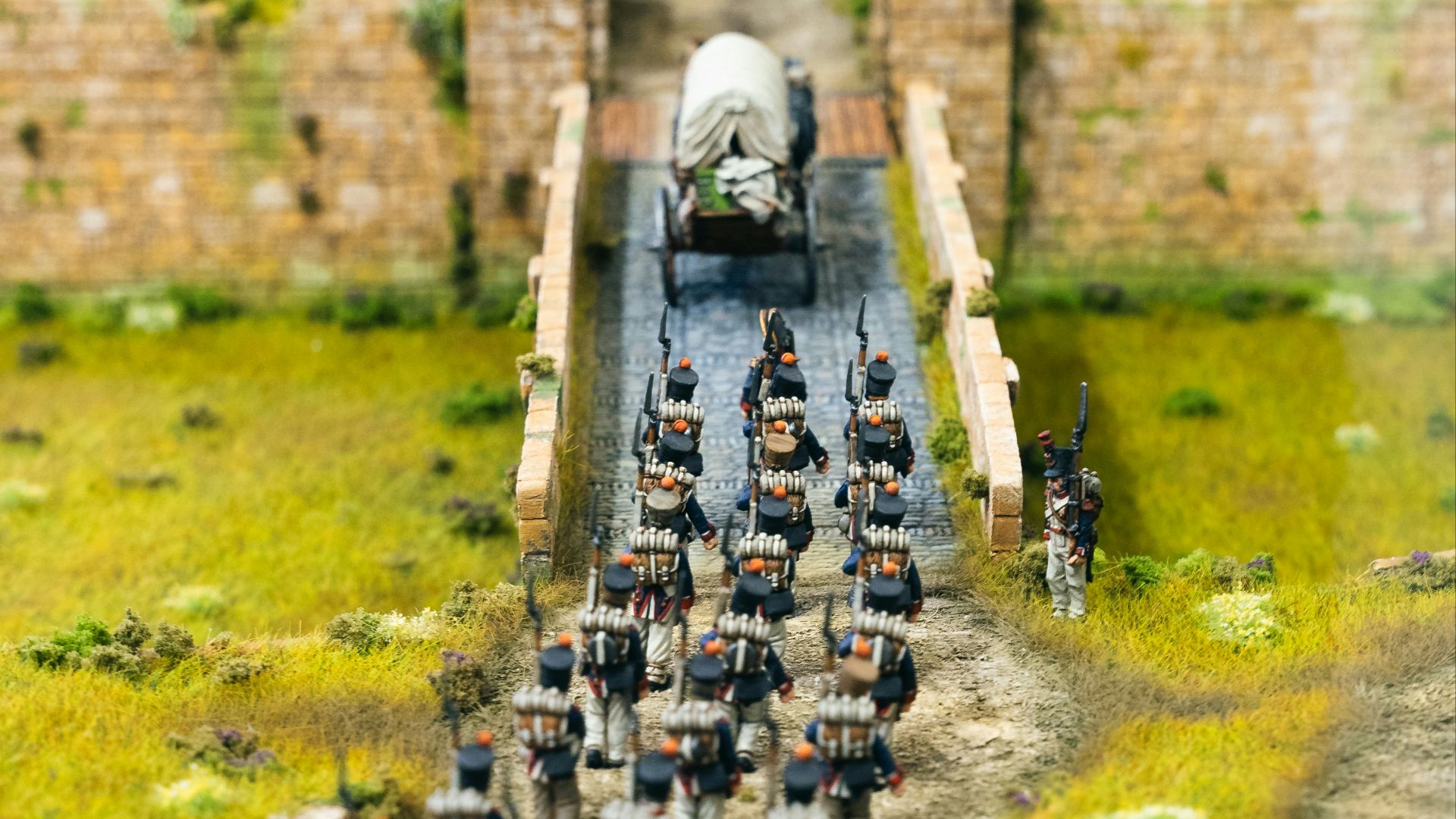 Soldiers march across a bridge towards a fortified entrance.