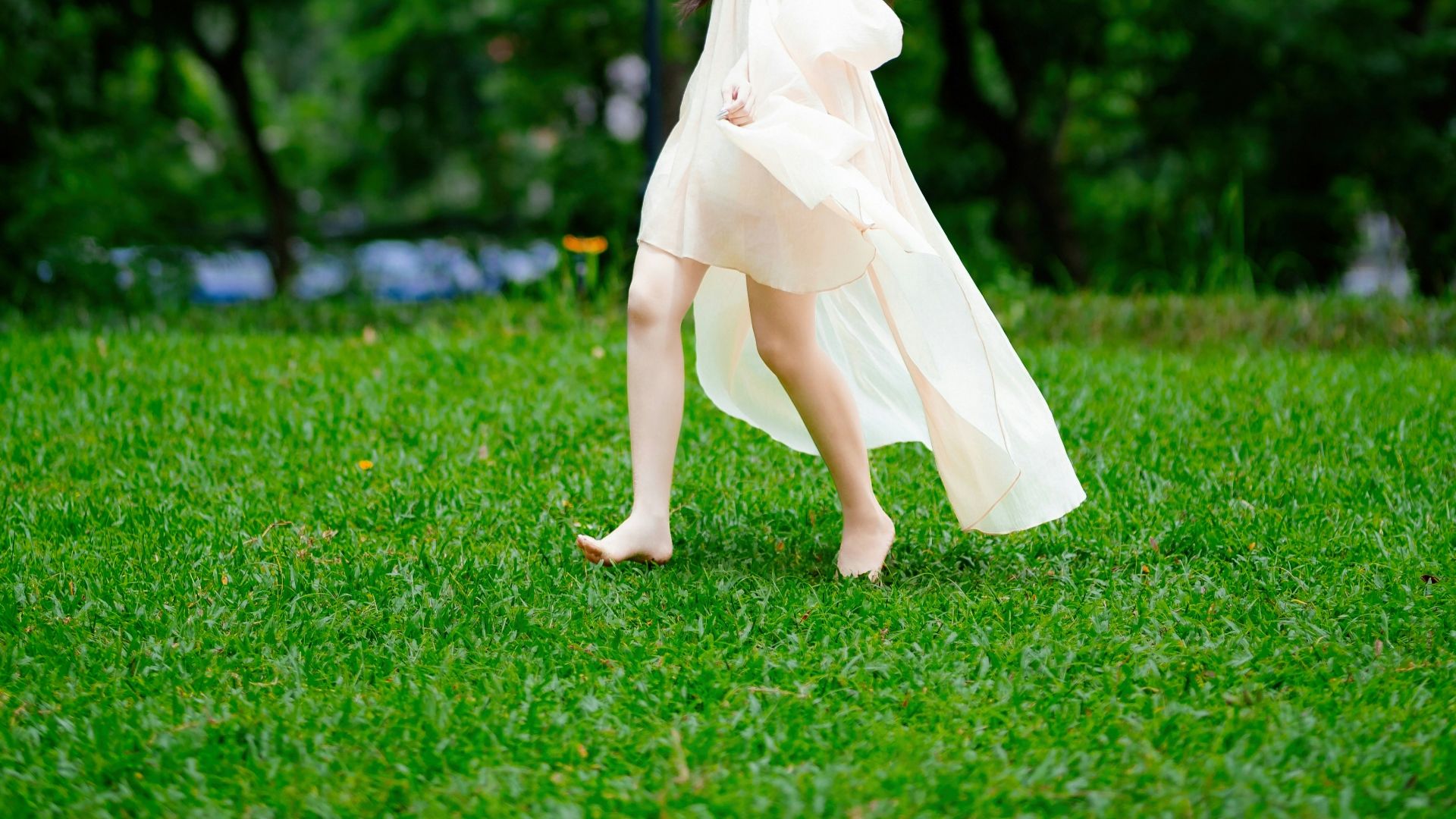 A woman in a flowing dress walks on grass.